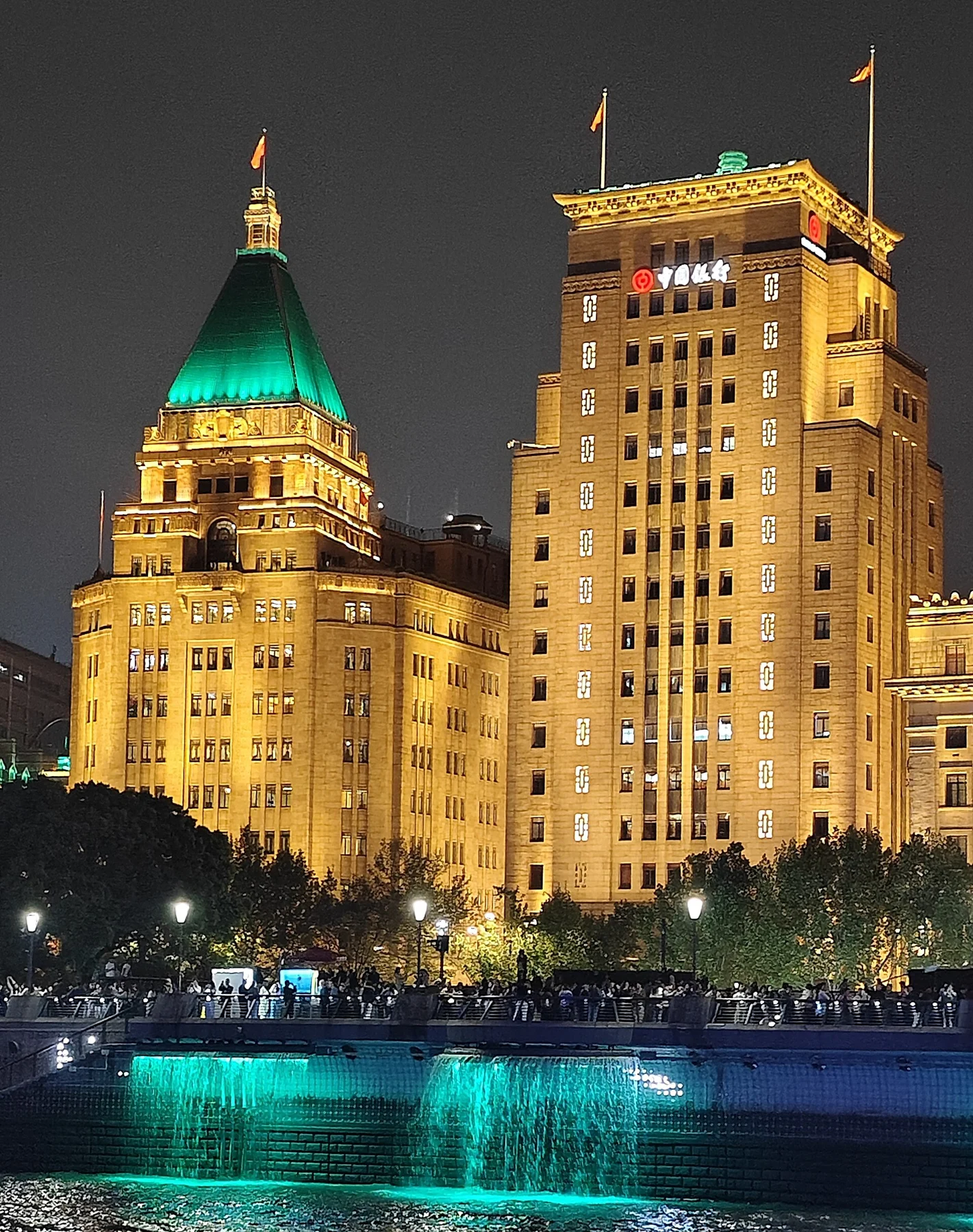 Illuminated hotel and bank facades against a dark sky, with the green hotel roof visible.