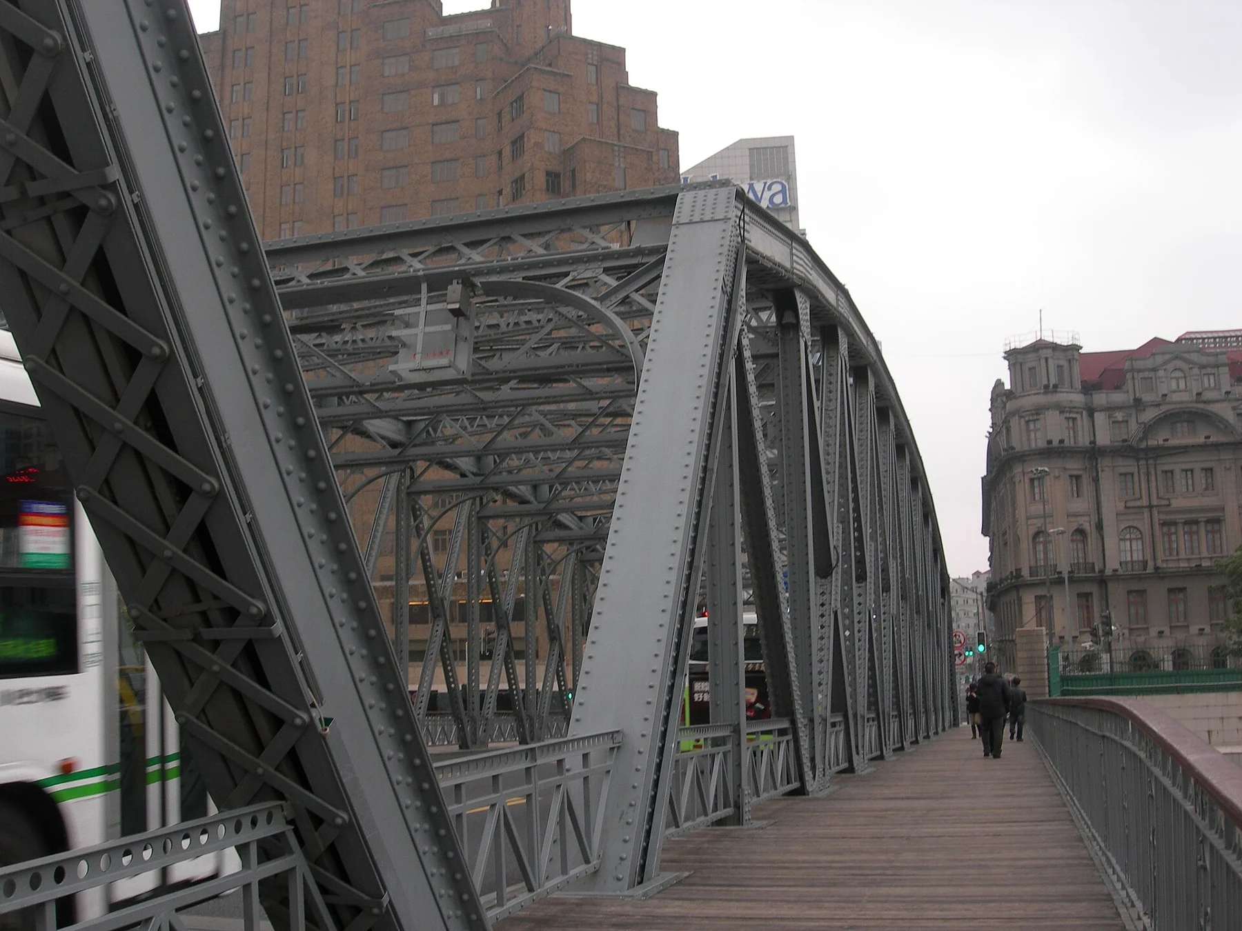 A pedestrian path beneath repeated steel bridge members, with people walking ahead.