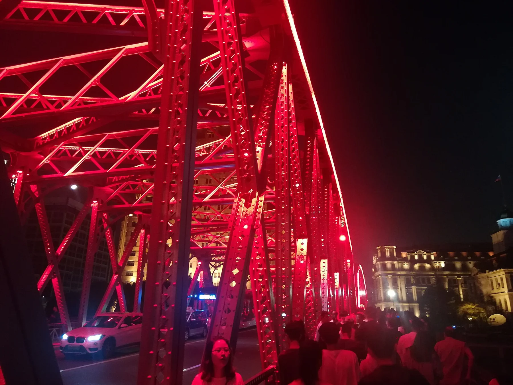 Red-lit steel bridge trusses above a pedestrian footway at night.