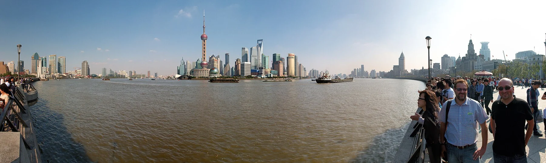 People on a riverfront promenade looking across the water towards the Pudong towers.