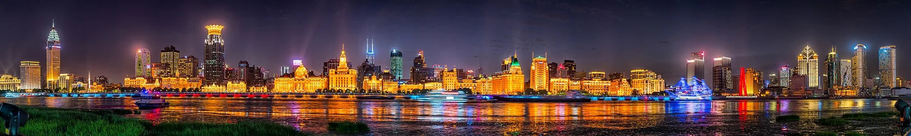 A long illuminated line of historic buildings along the river under a dark sky.
