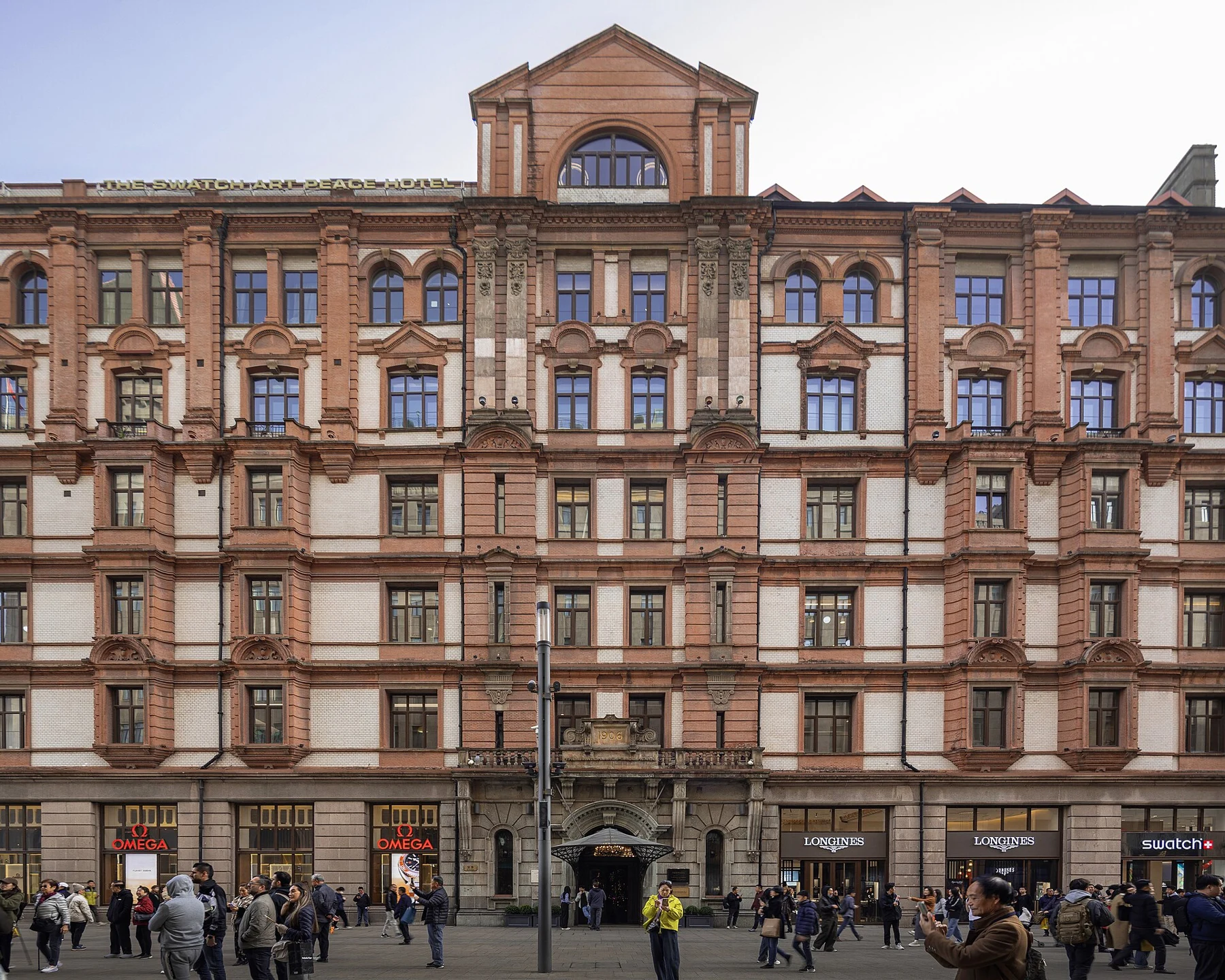 A red-brick-and-pale-stone hotel facade with arched upper windows and people at street level.