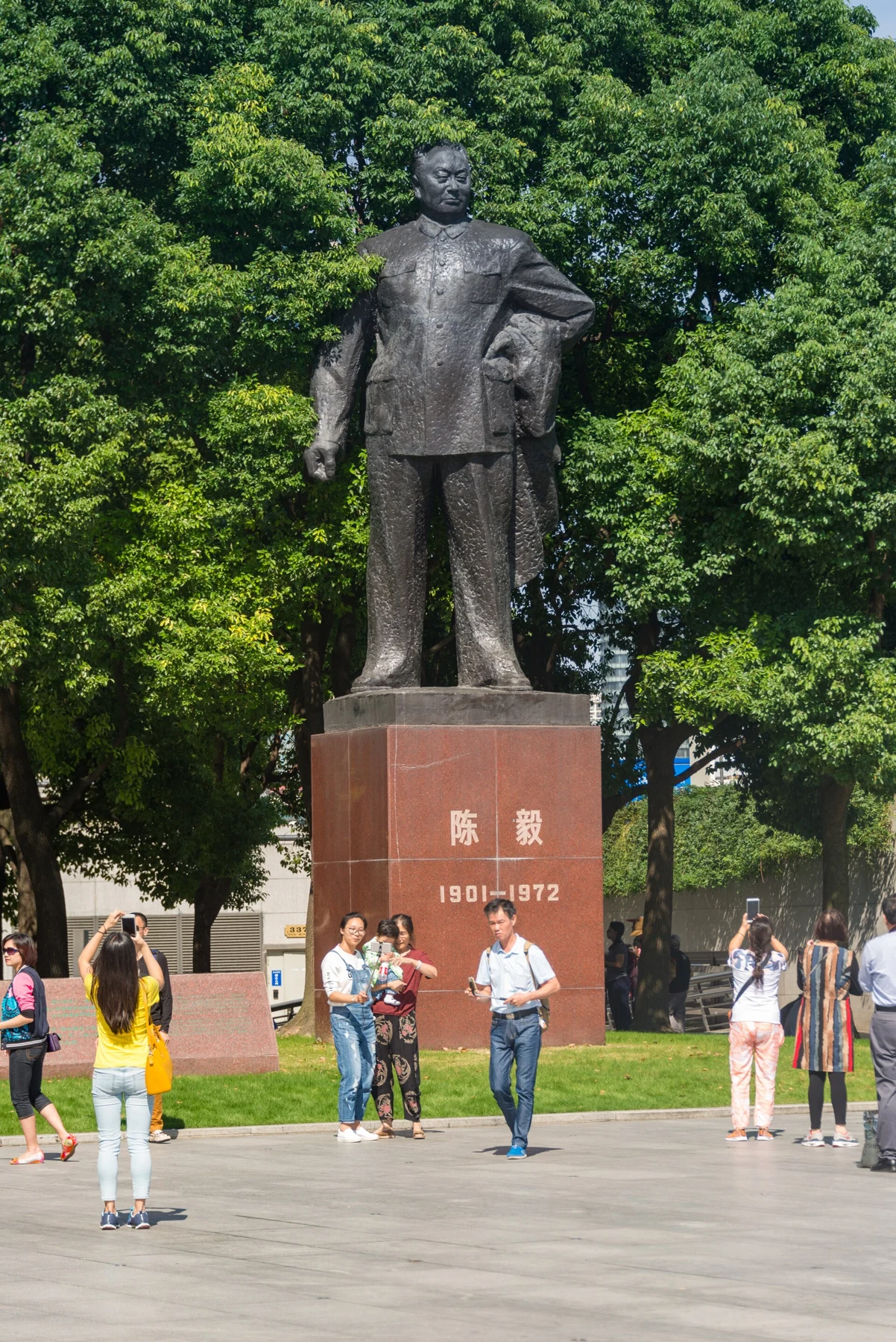 A standing statue labelled 陈毅, with visitors and leafy trees behind it.