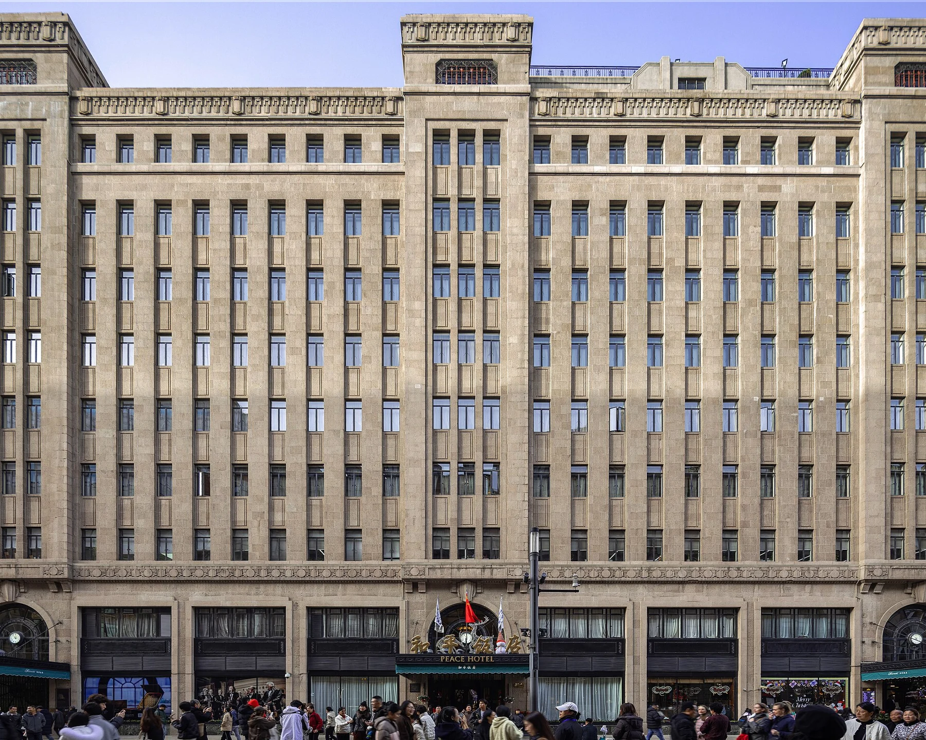 A long stone hotel facade with repeated windows and people on the pavement.