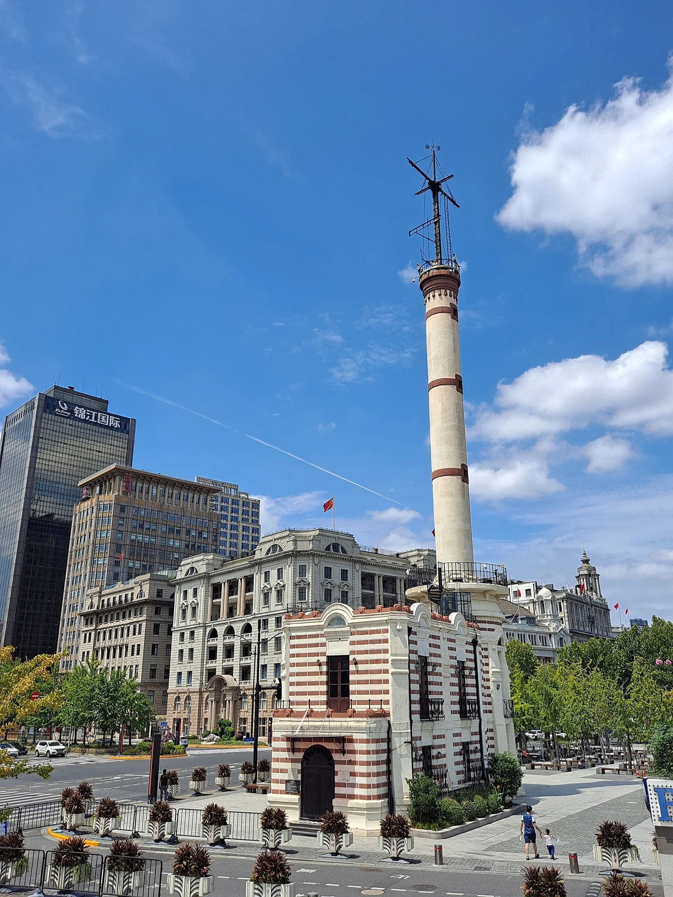 A narrow striped tower with a rounded top and tall signal mast by the riverfront.