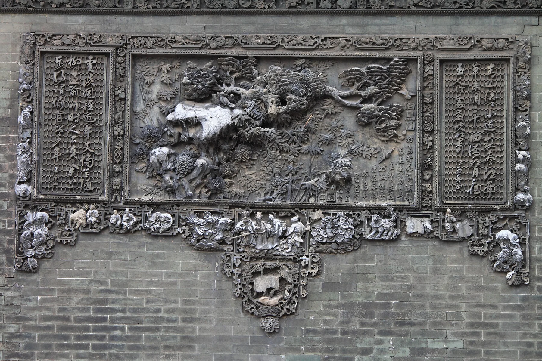 Grey brick relief of birds and plants with carved inscriptions at the sides.