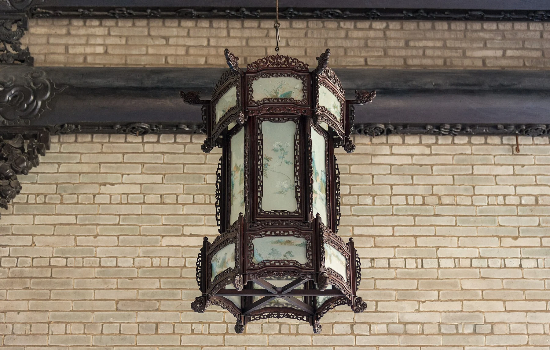 Tall hanging lantern against a brick wall and dark horizontal beam.