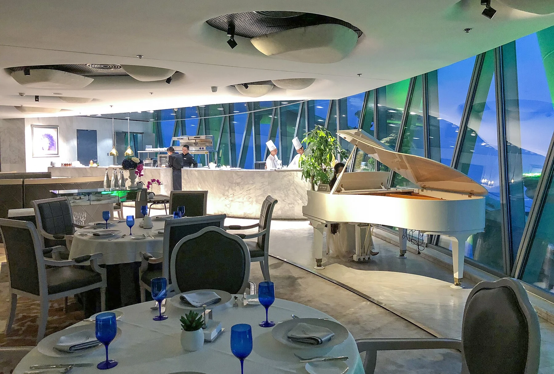 Dining tables, blue glasses and a piano in a high-level restaurant interior.