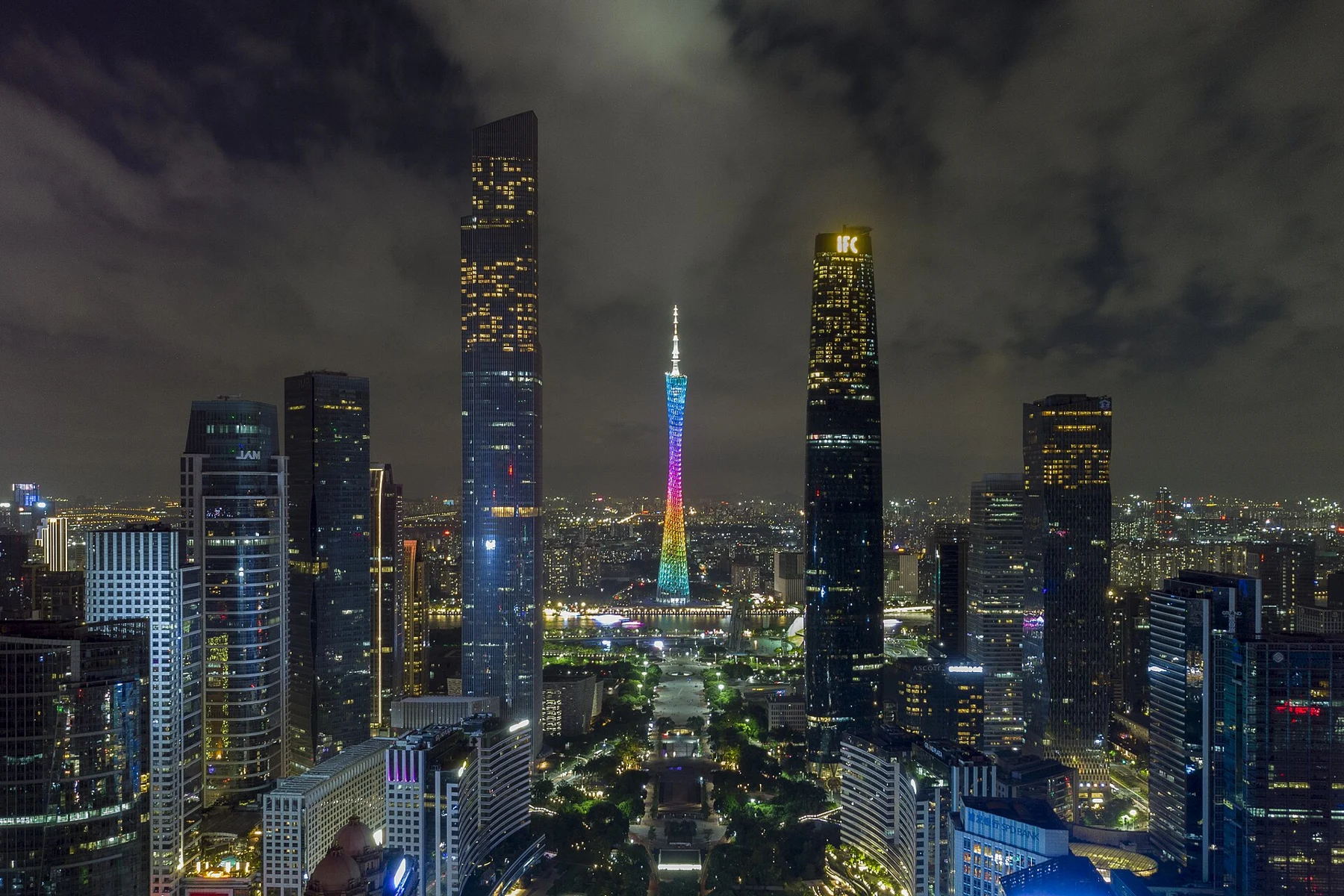 Illuminated tower and river seen between nearby city buildings at night.