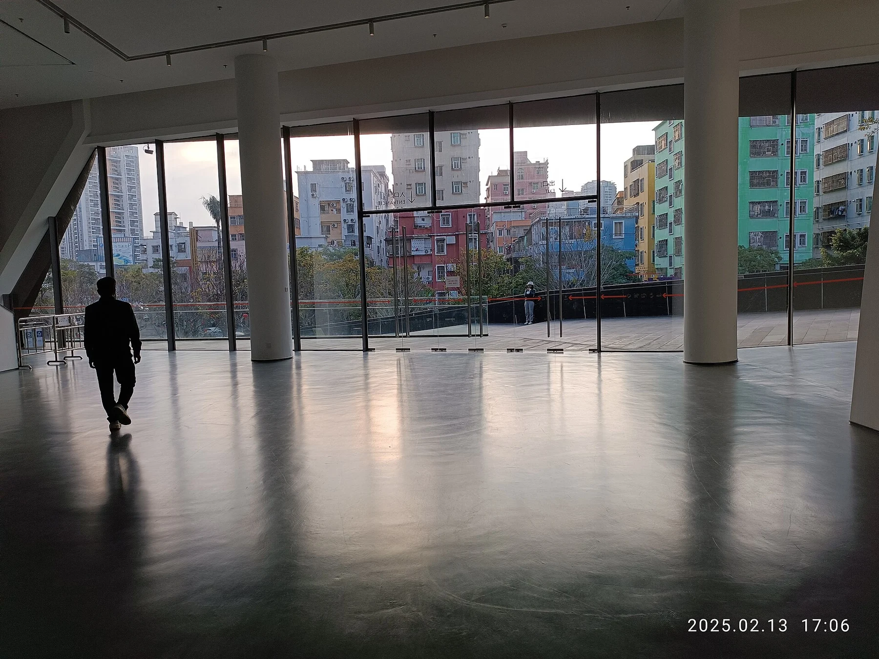 Open museum entrance area with columns, large glass doors and neighbourhood buildings beyond