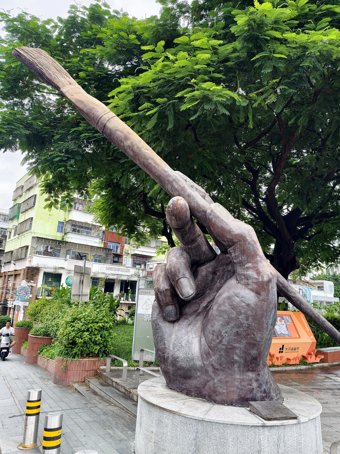 Oversized sculpted hand gripping a paintbrush against leafy trees
