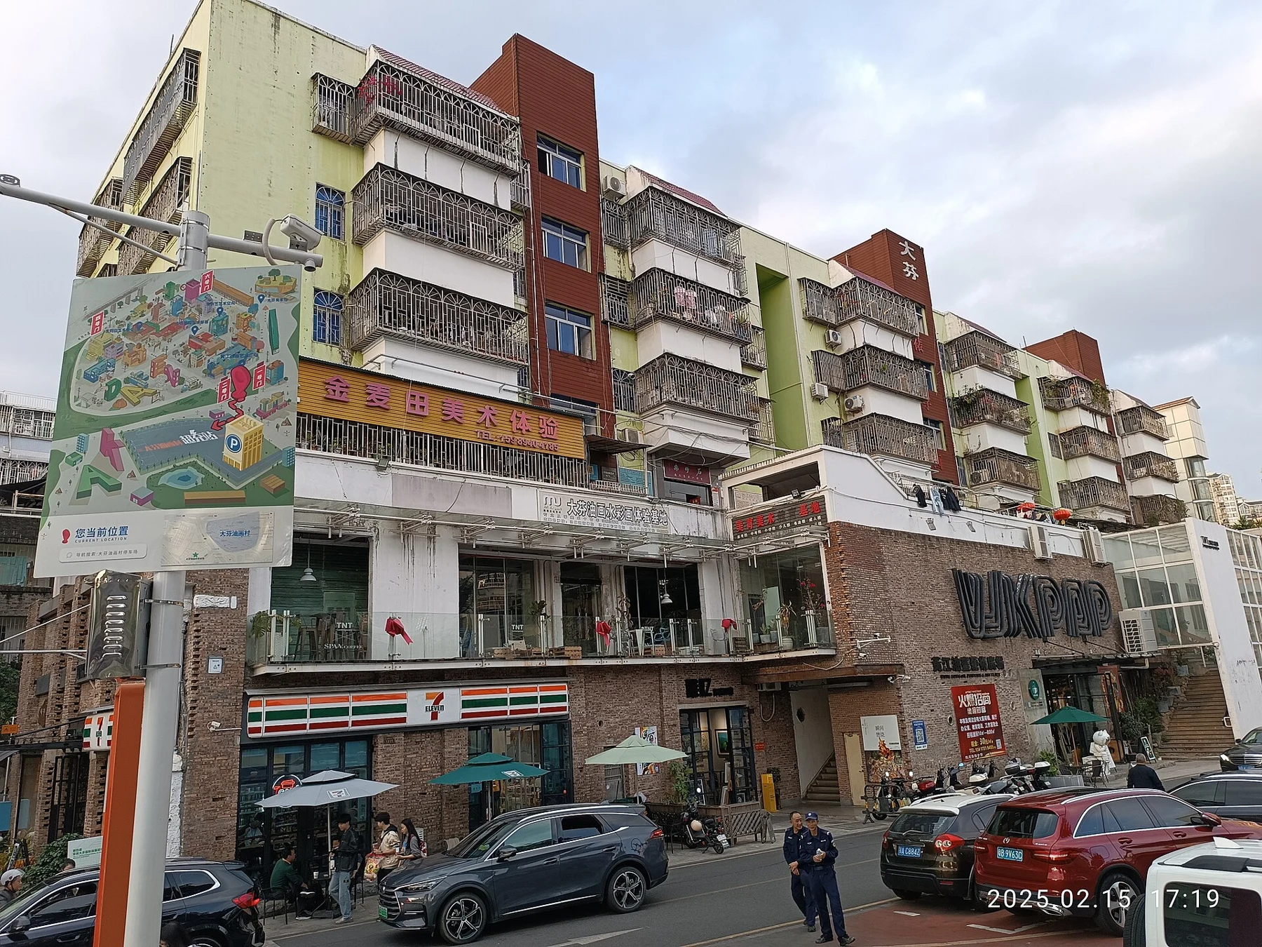 Multi-storey Dafen streetfront with studio signs, shops, balconies and vehicles