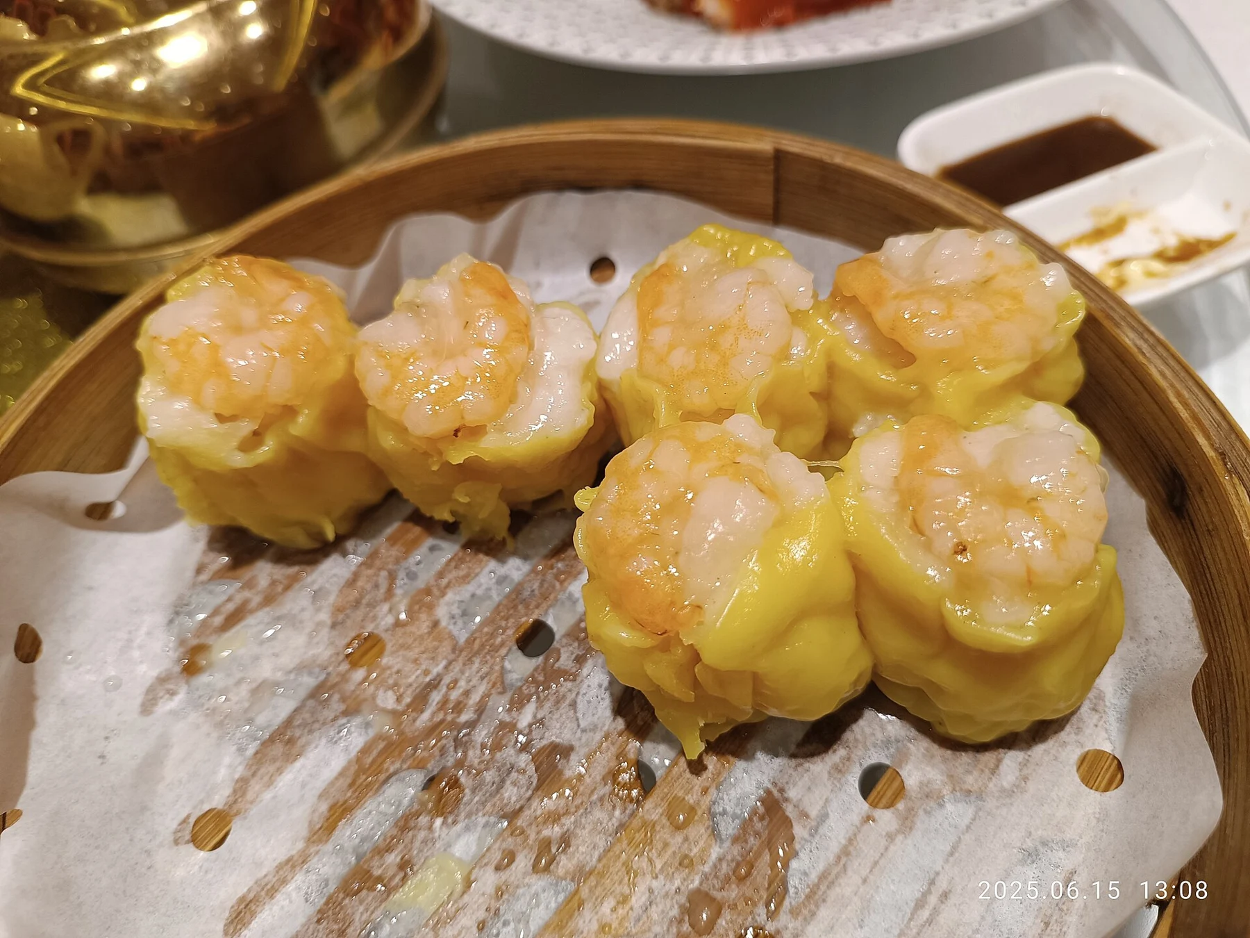 Yellow-wrapped siu mai topped with prawns in a bamboo steamer