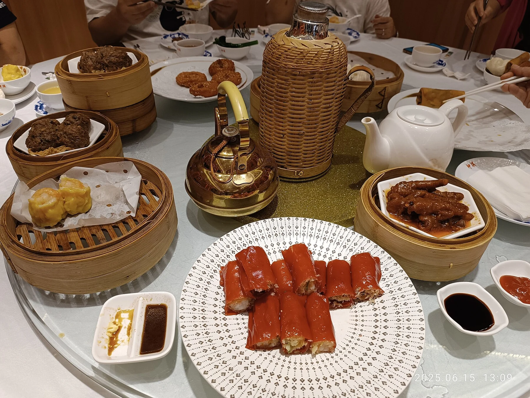 A restaurant table with tea, bamboo baskets of dim sum and a plate of red rice rolls