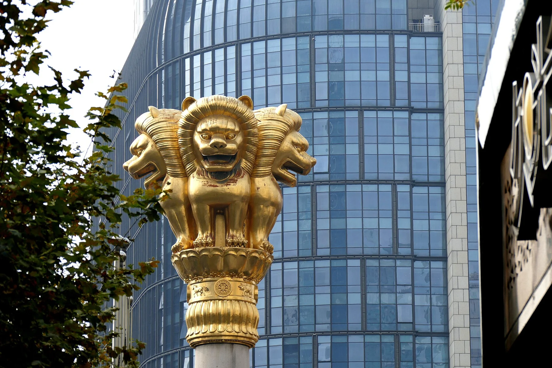 Lion heads and paws arranged around a decorated capital against a modern building.