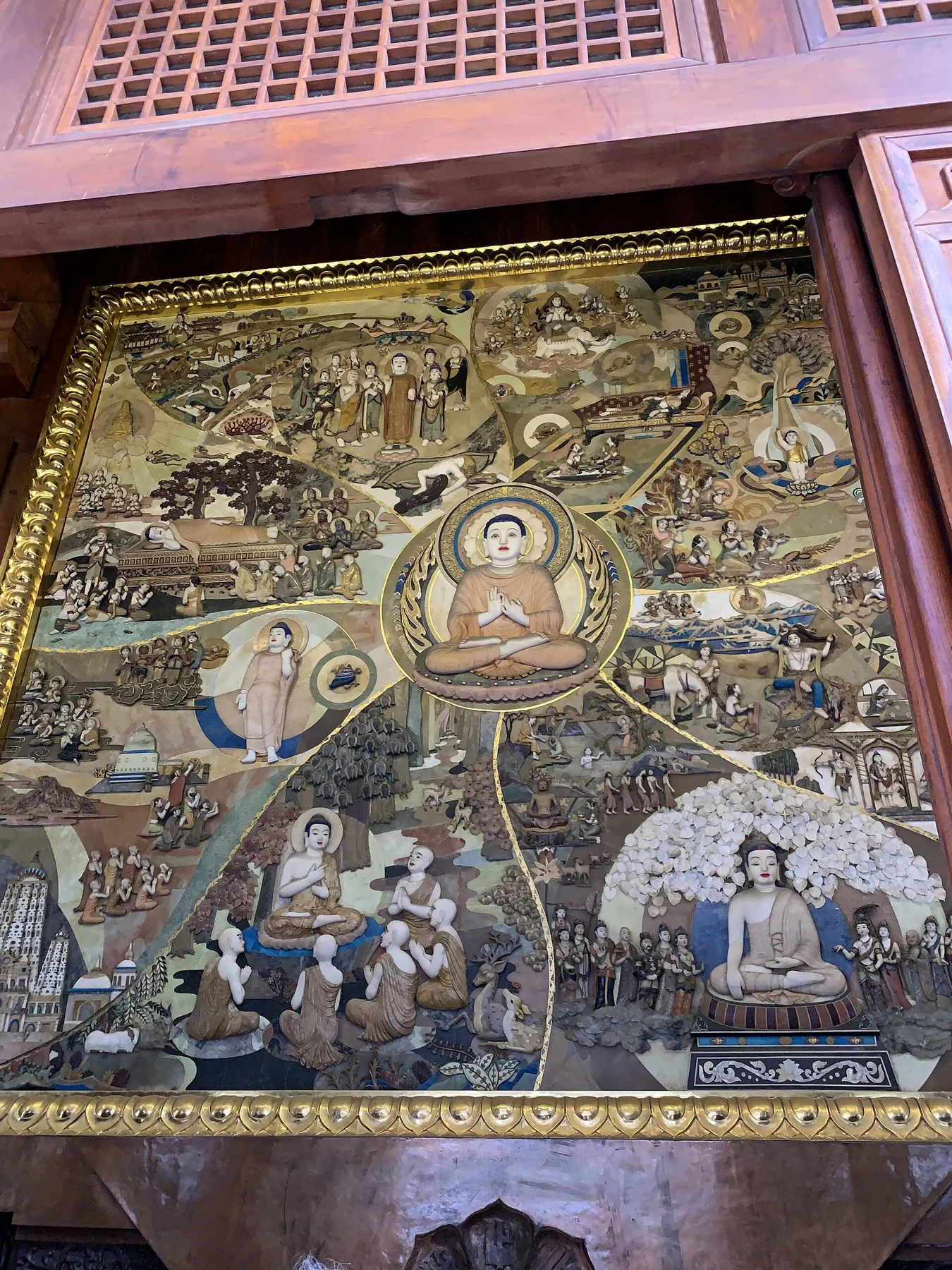 Narrative panel with figures, trees and architectural scenes around a central seated Buddha.