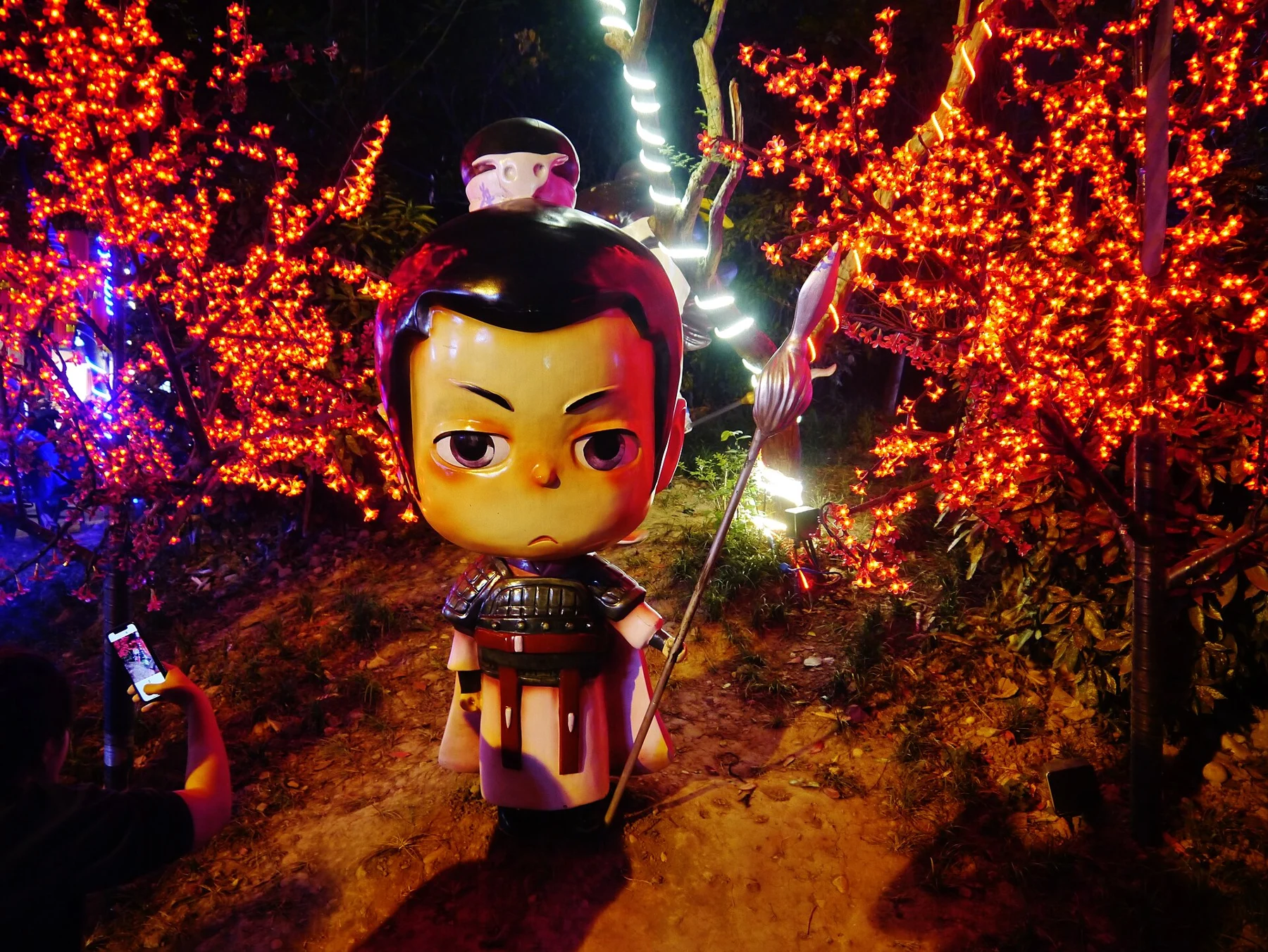 Large stylised character figure with an oversized head among illuminated trees
