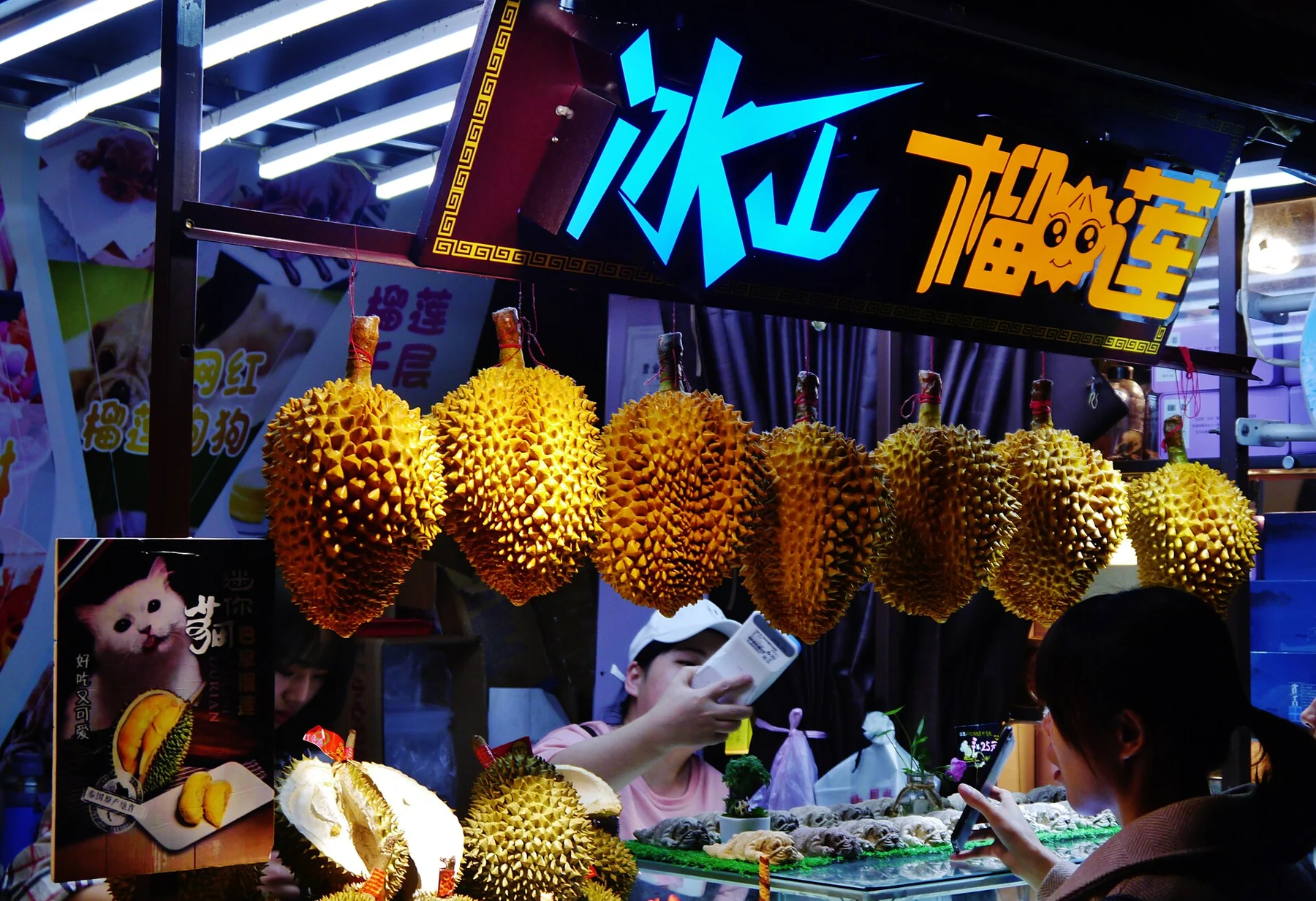 Durian fruits hanging above a brightly lit food counter