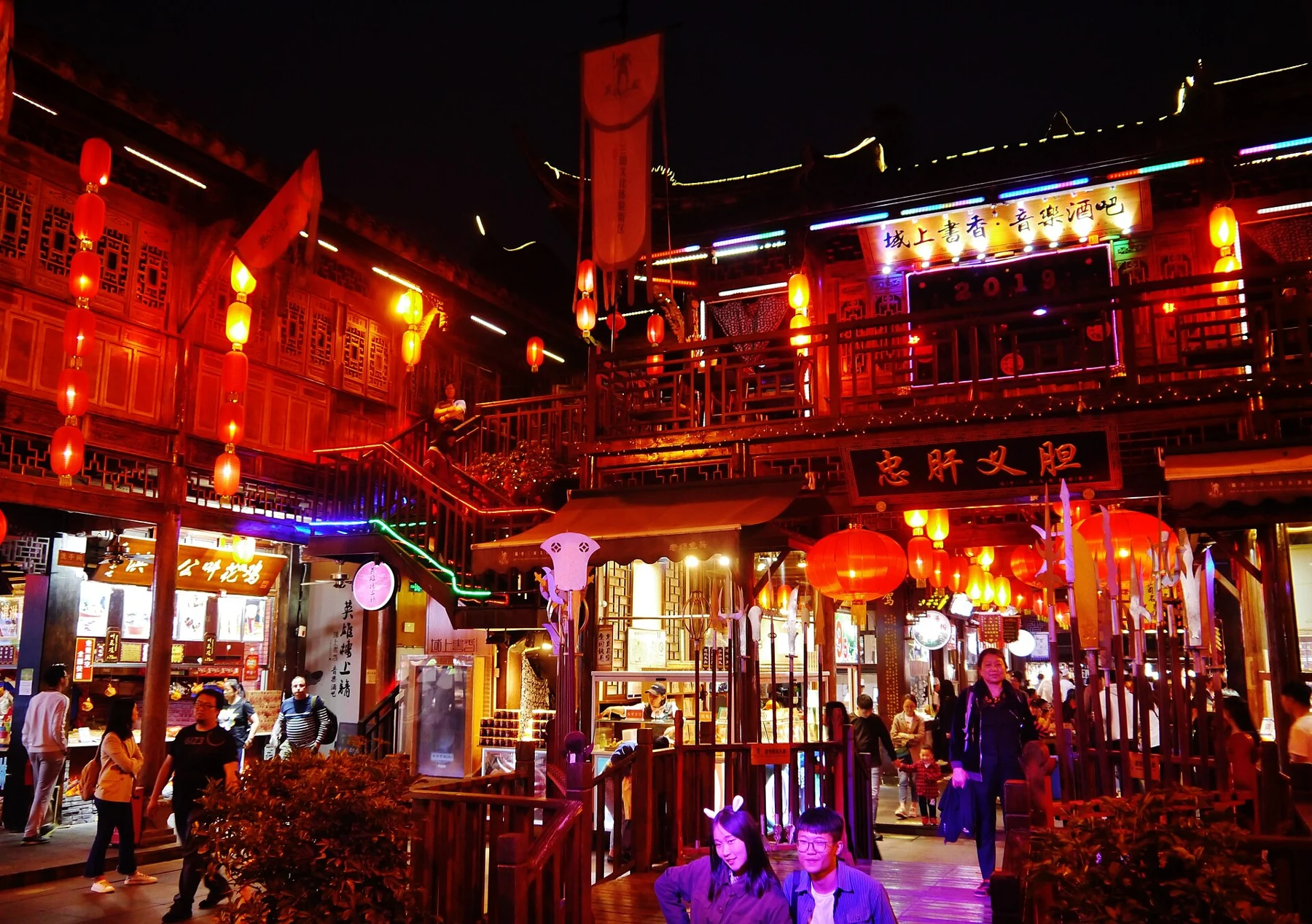 Illuminated timber connection over a lane of shops and visitors
