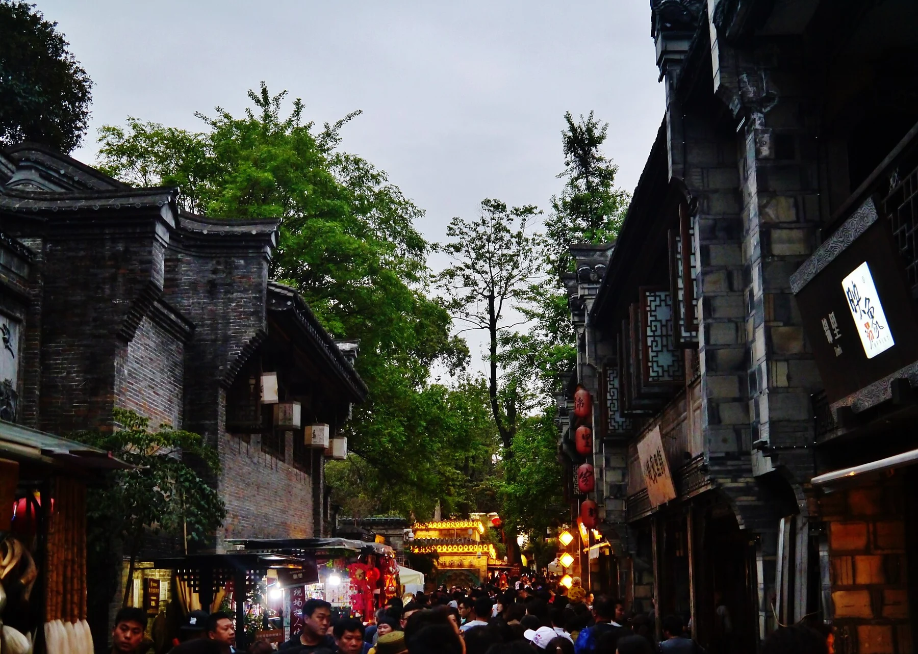 Grey-tiled roof lines and trees above a lane of visitors