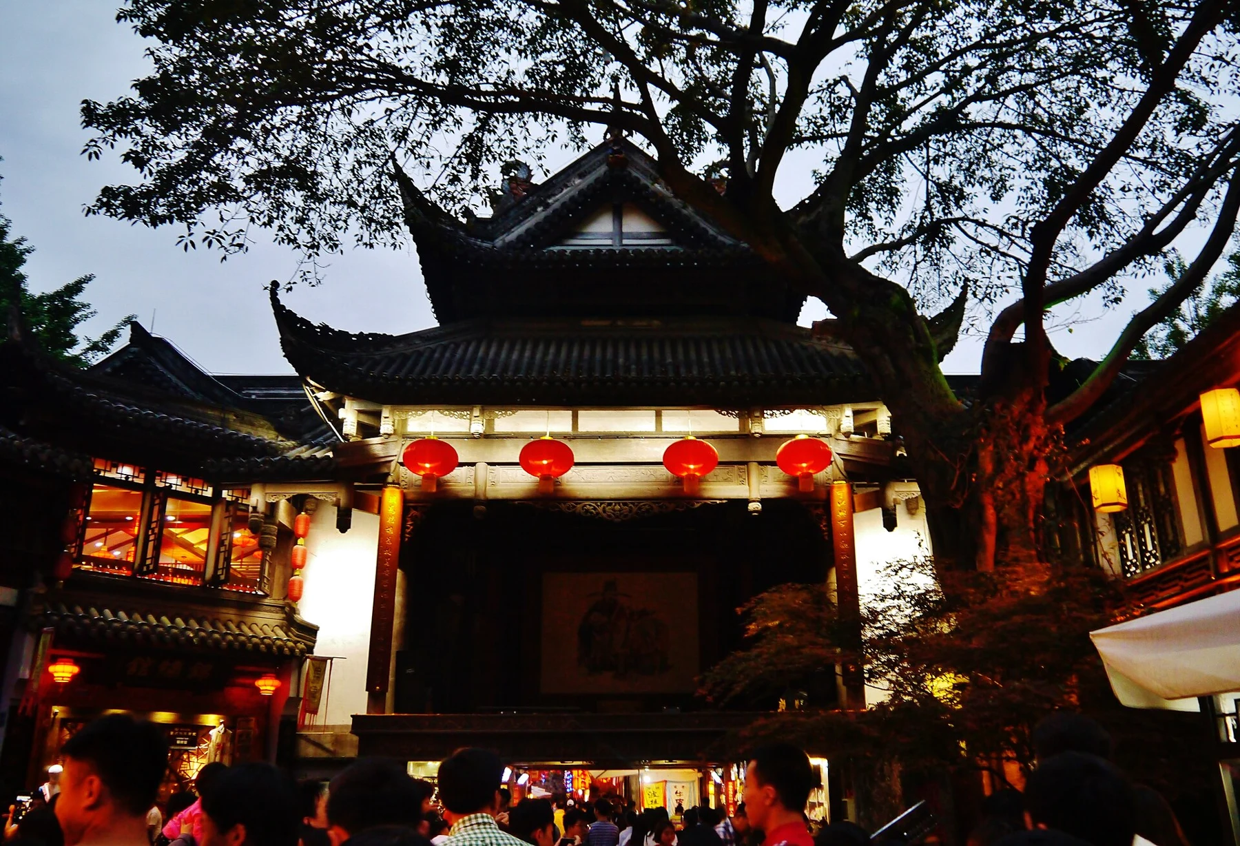 Traditional theatre-stage front beneath a tree with lanterns below its eaves