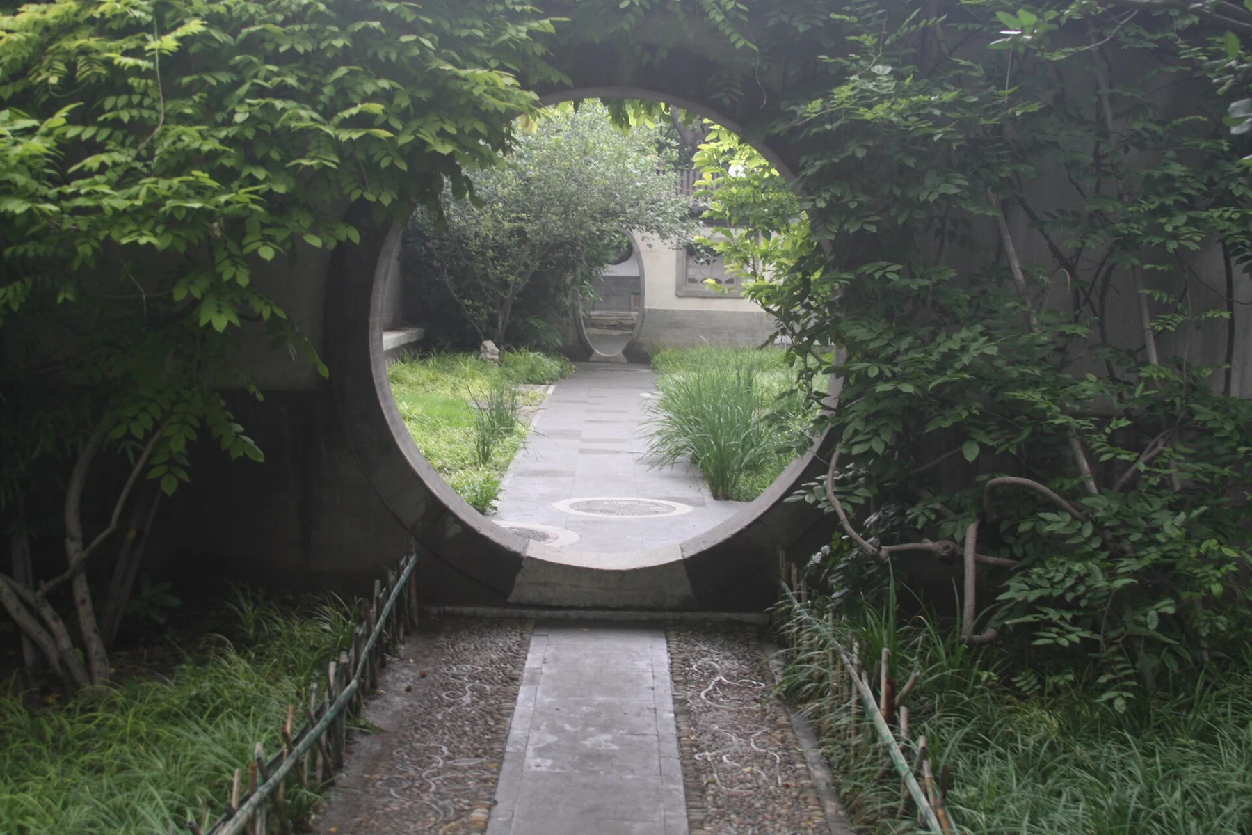 One circular moon gate framing another across a planted garden path.
