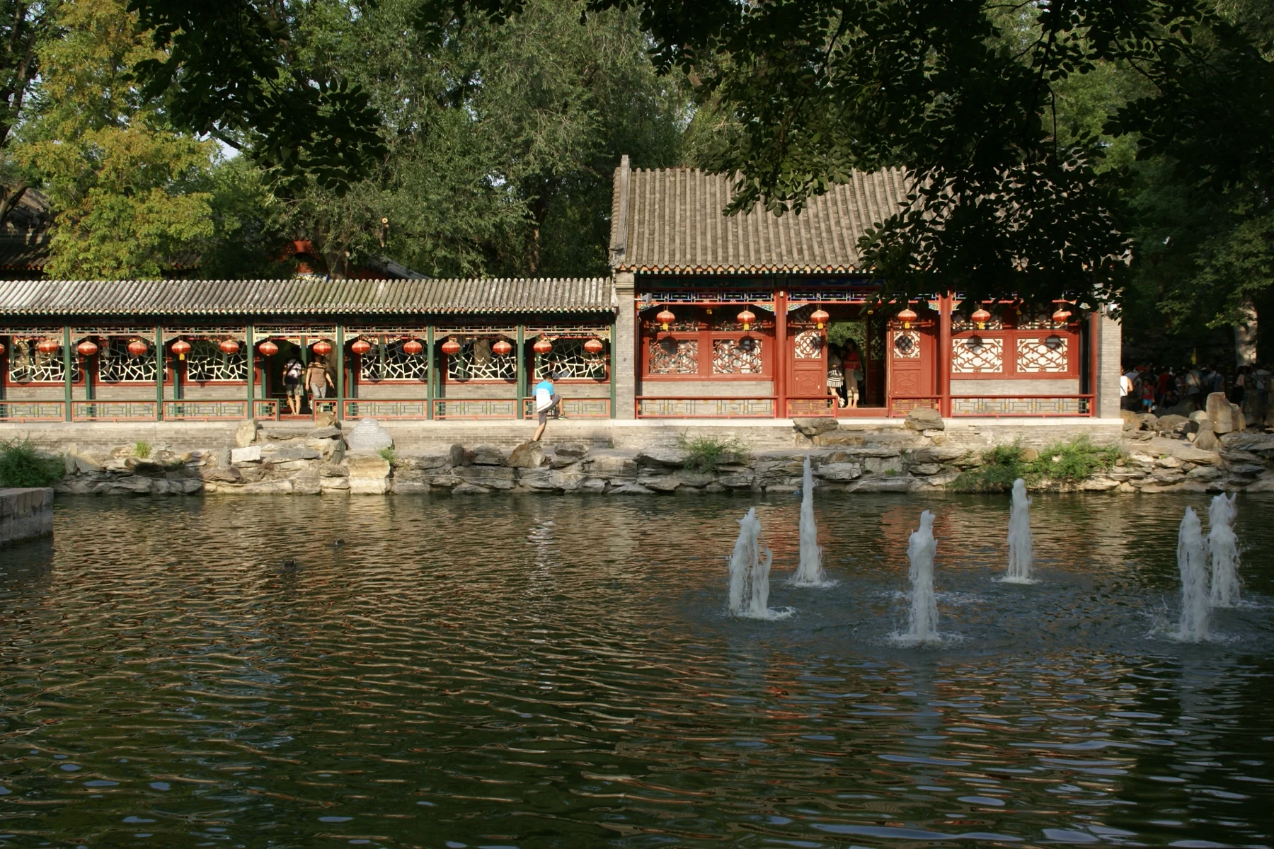 A garden pool with low rock edges and red pavilions beyond.