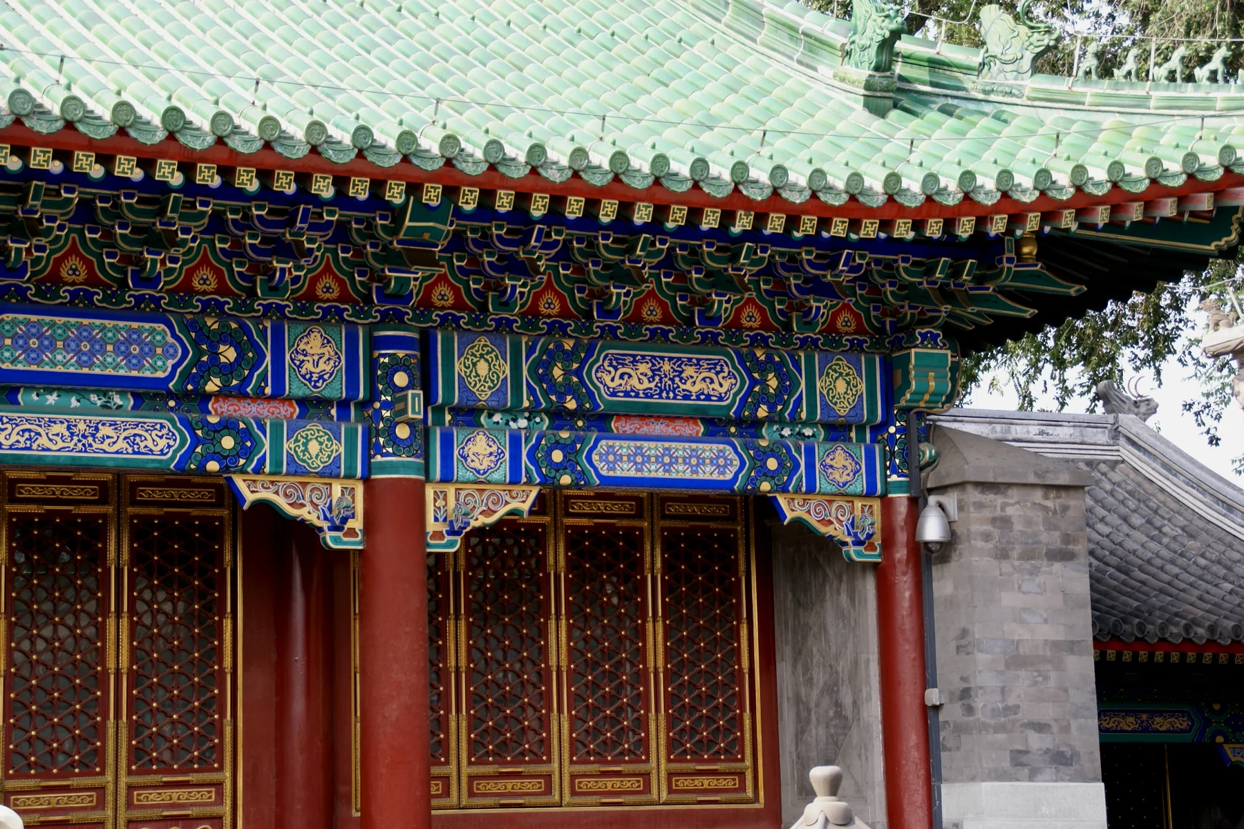 A close view of green glazed tiles, colourful painted brackets and red lattice doors.