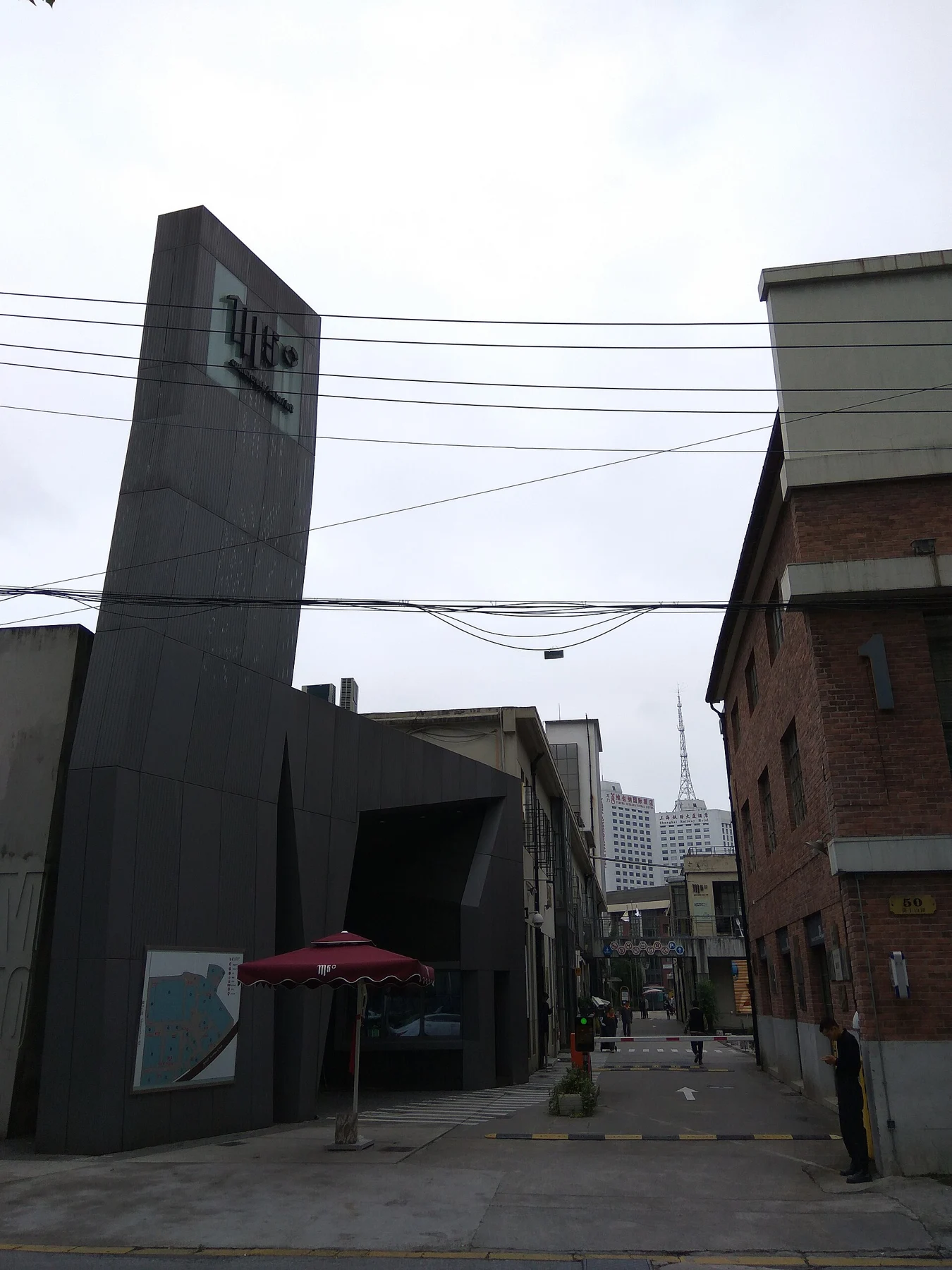 A tall dark entrance structure beside brick buildings and an open passage.