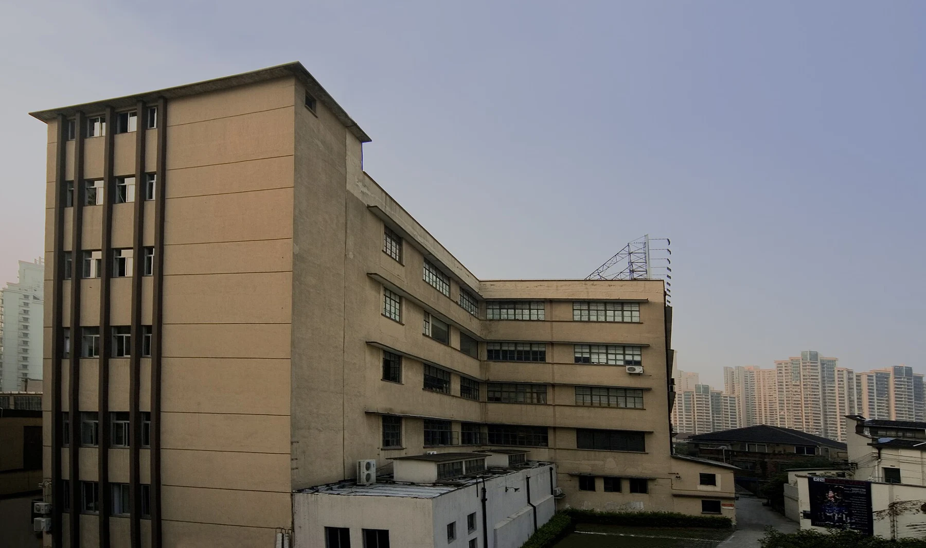 A pale multi-storey industrial building with rows of windows and a lower adjoining wing.