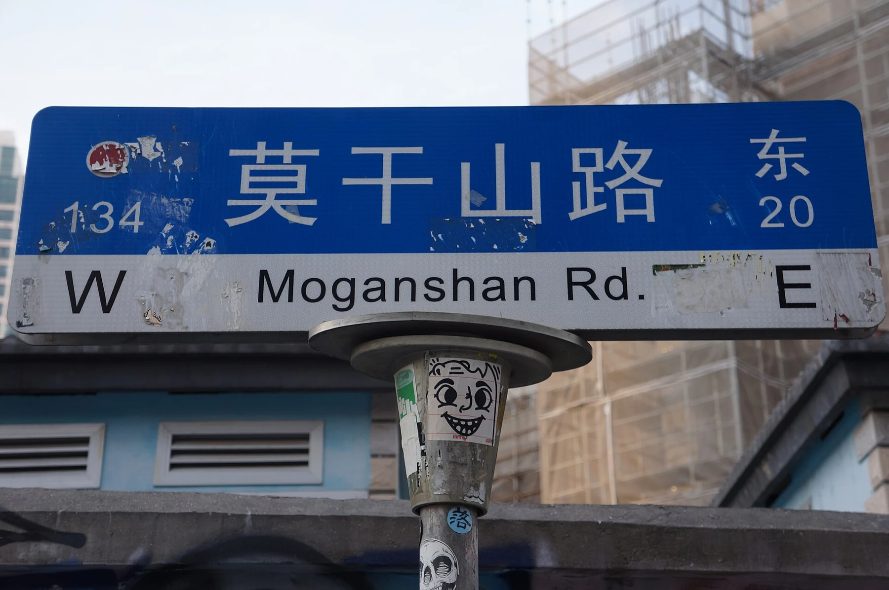 A blue 莫干山路 Moganshan Road street sign above a sticker-covered pole.