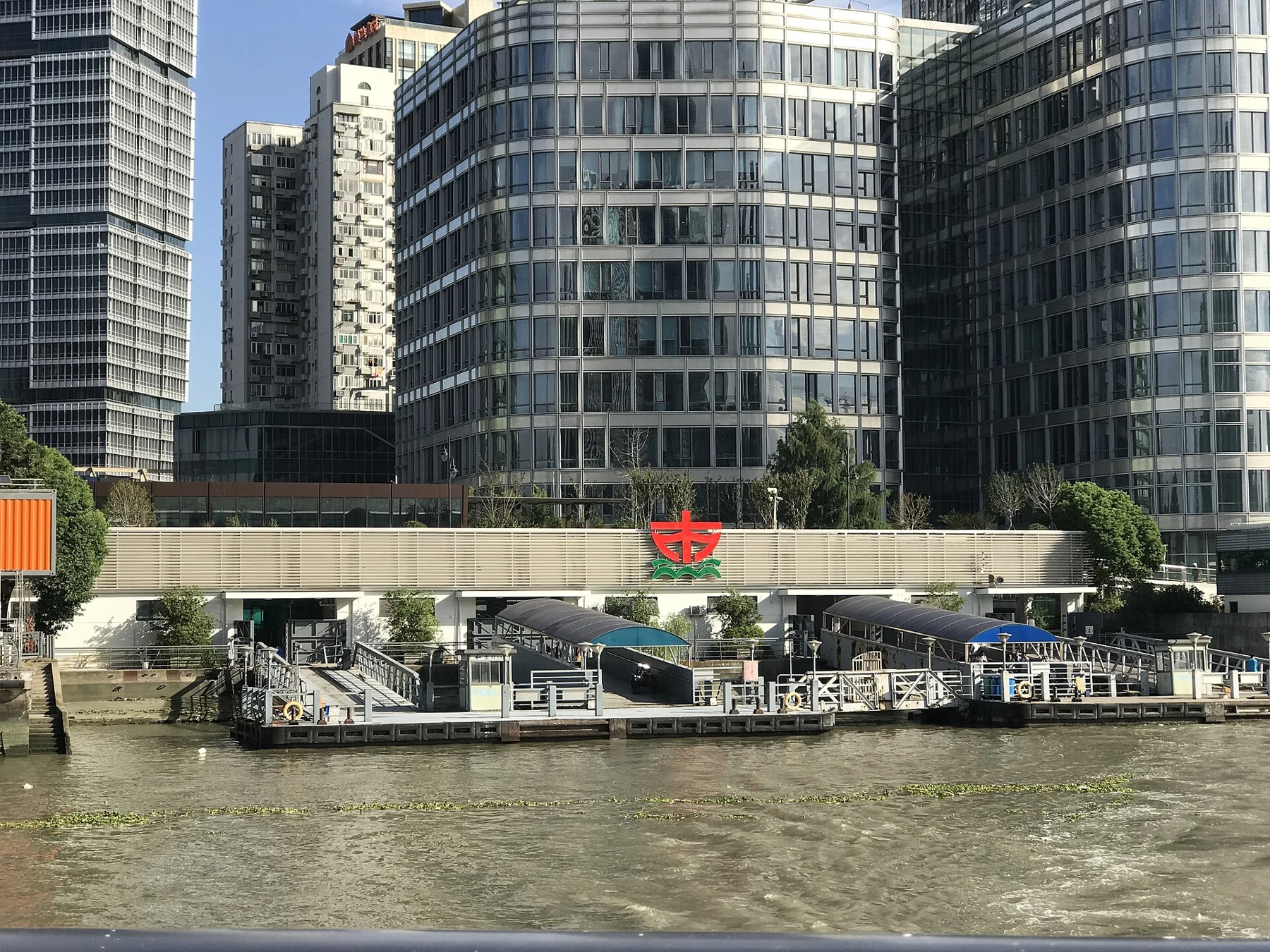 A low ferry-terminal structure bearing a red star in front of modern office buildings.
