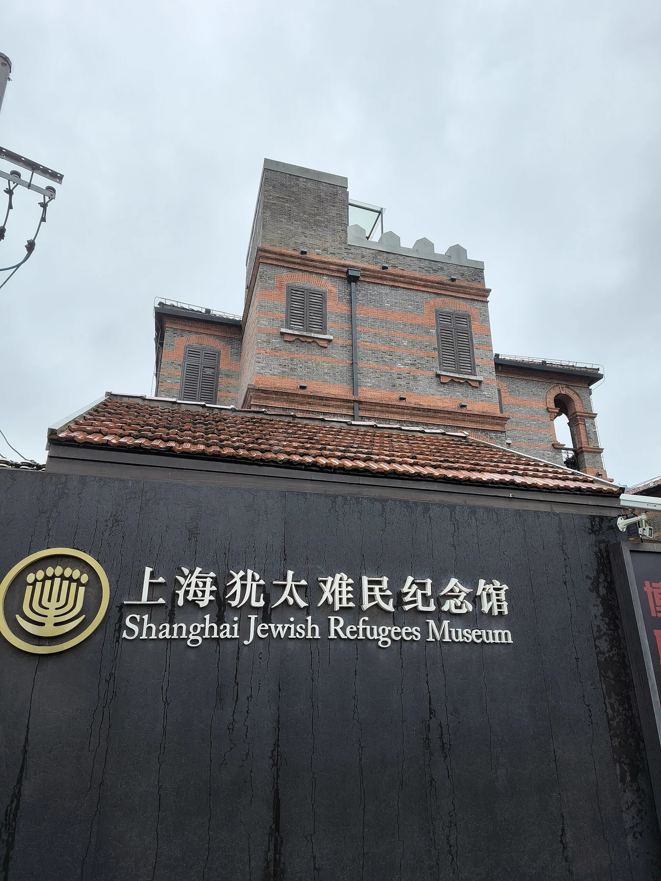 A dark sign reading Shanghai Jewish Refugees Museum below a red-and-grey brick façade.