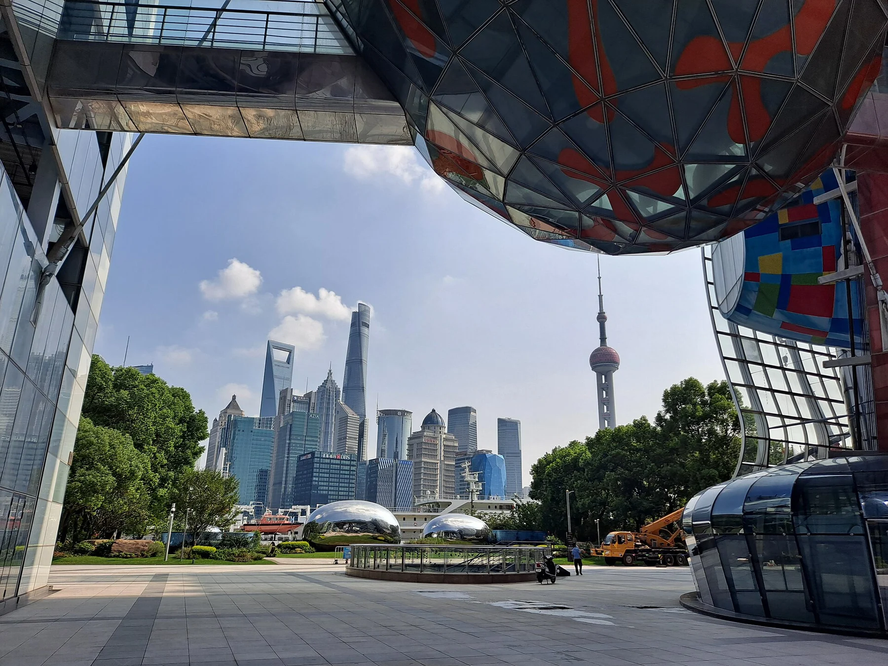 The skyline across the river framed by large structural legs and a suspended colourful rounded form.