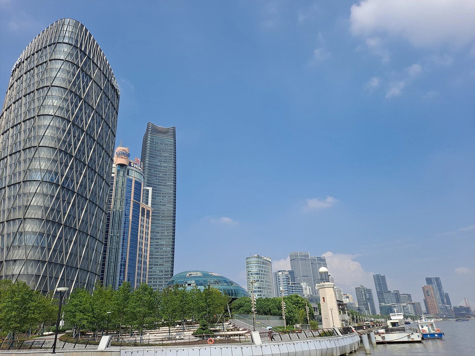 Modern riverfront buildings, planted public space and boats beside the embankment.