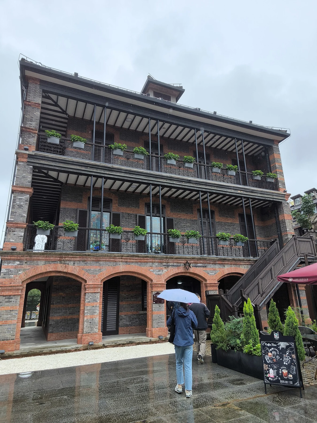 A brick courtyard building with timber upper galleries and a visitor holding an umbrella.