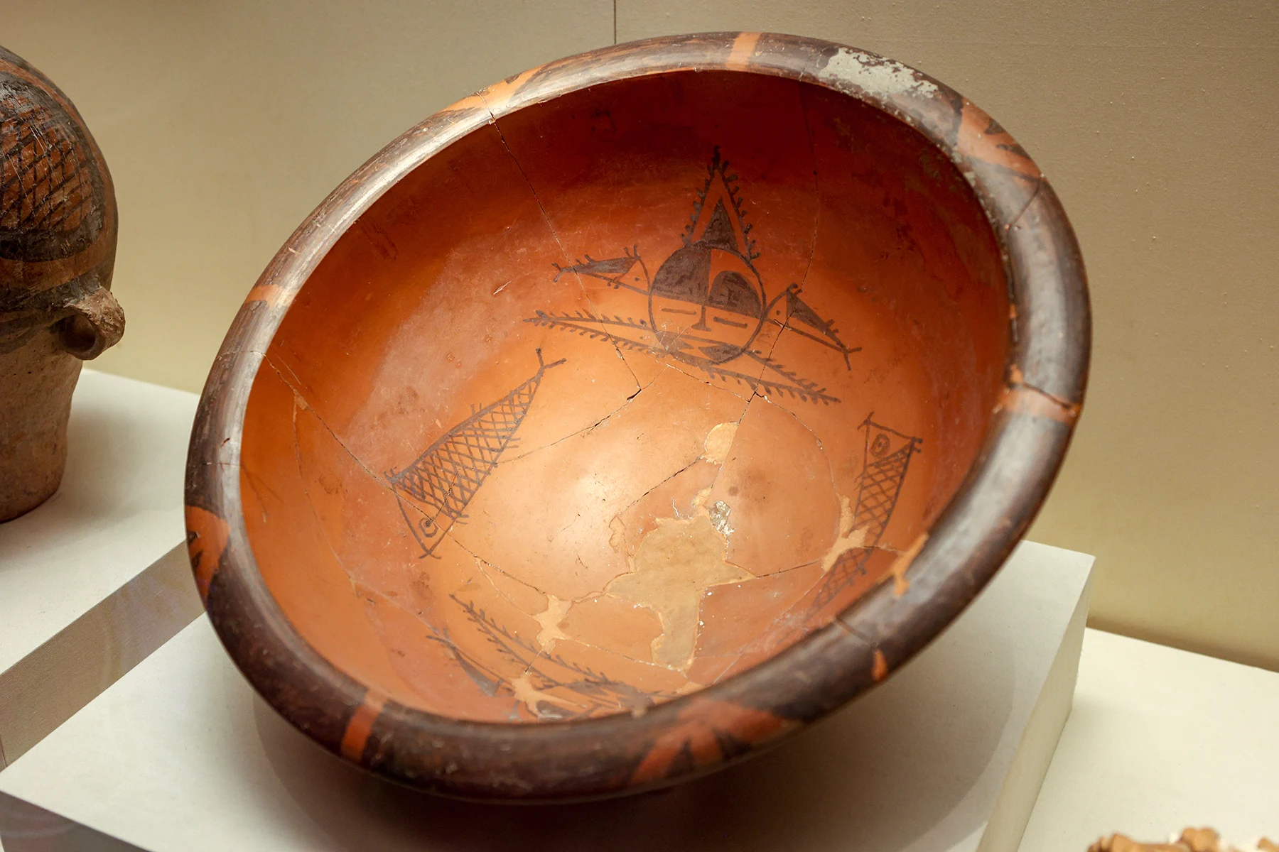 The inside of a painted pottery basin showing dark human-face and fish patterns.