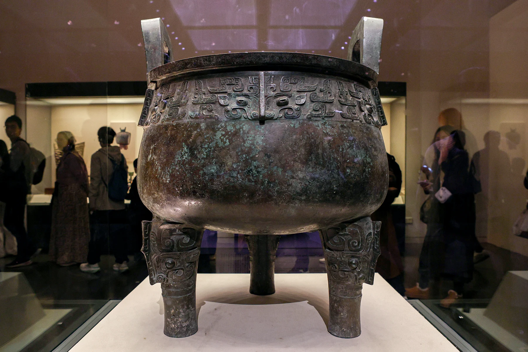 A large round bronze cauldron with two upright handles and three legs.