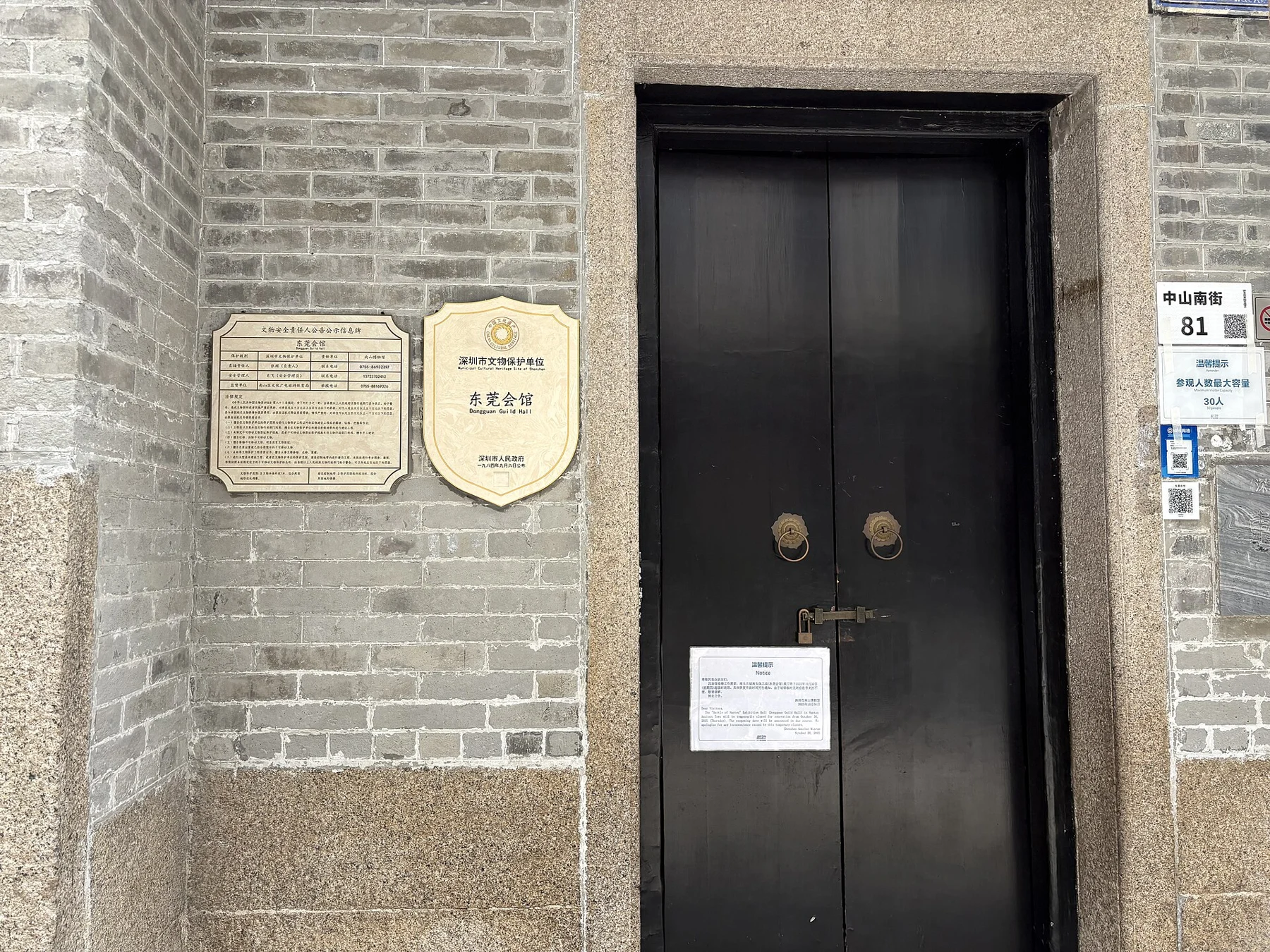 Closed dark timber exhibition door with a renovation notice, heritage plaque and number 81
