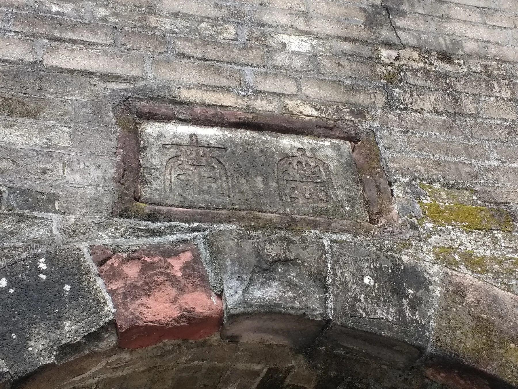 A weathered inscribed stone set into the masonry above an arch