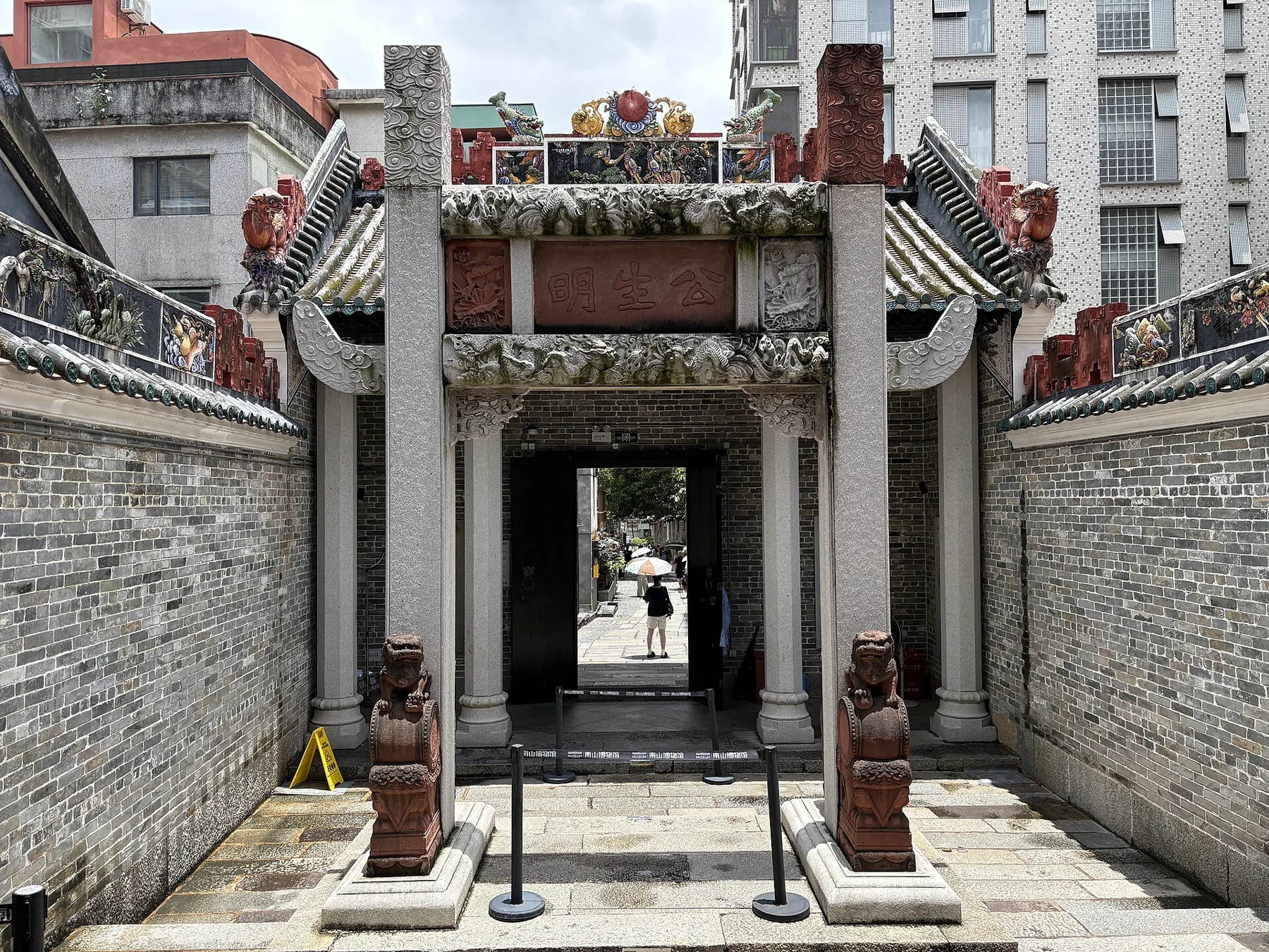 Decorated courtyard entrance with columns, carved panels, stone lions and the maxim 公生明
