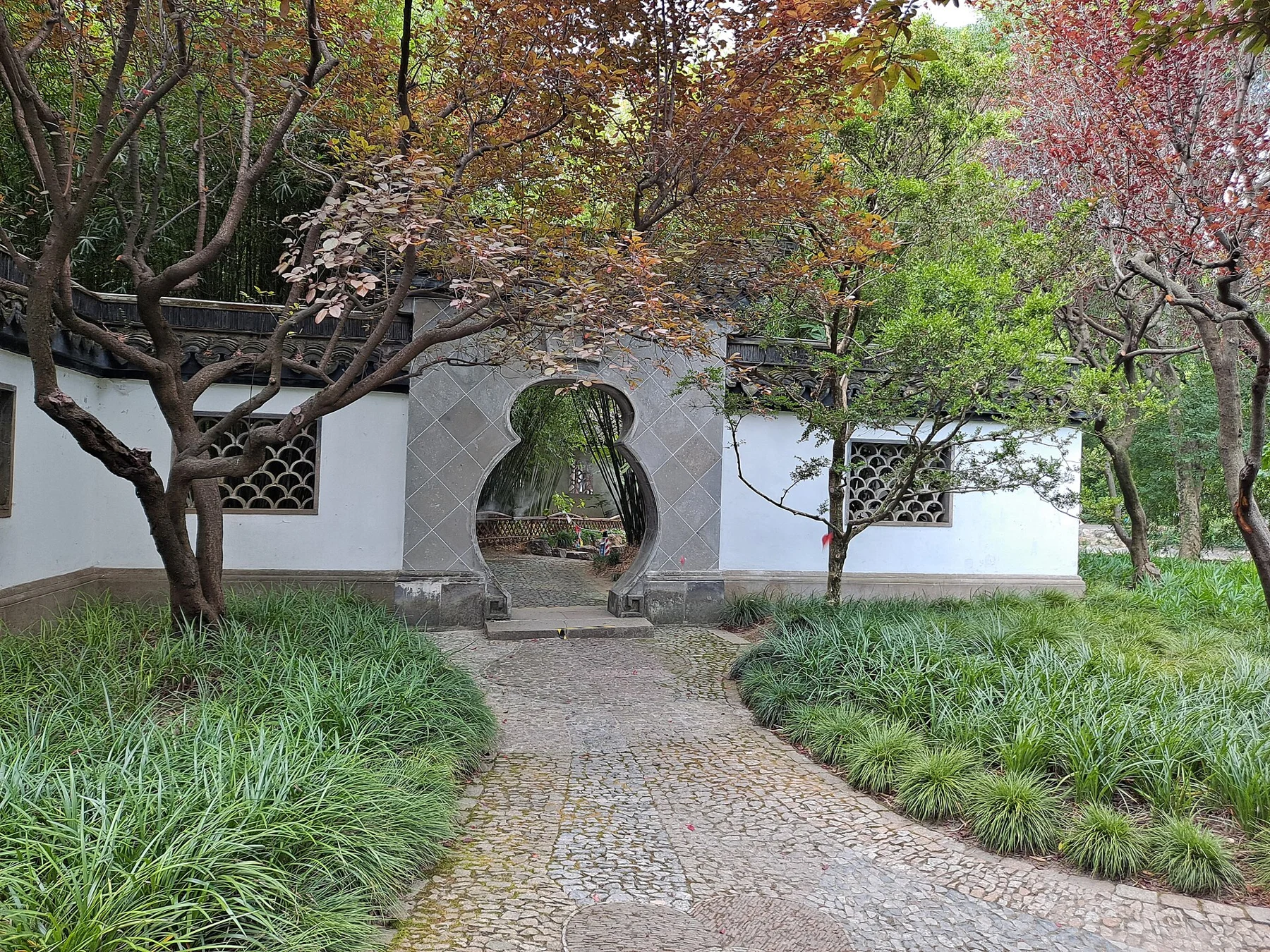 A gourd-shaped opening through a white wall, framed by trees and a patterned path.