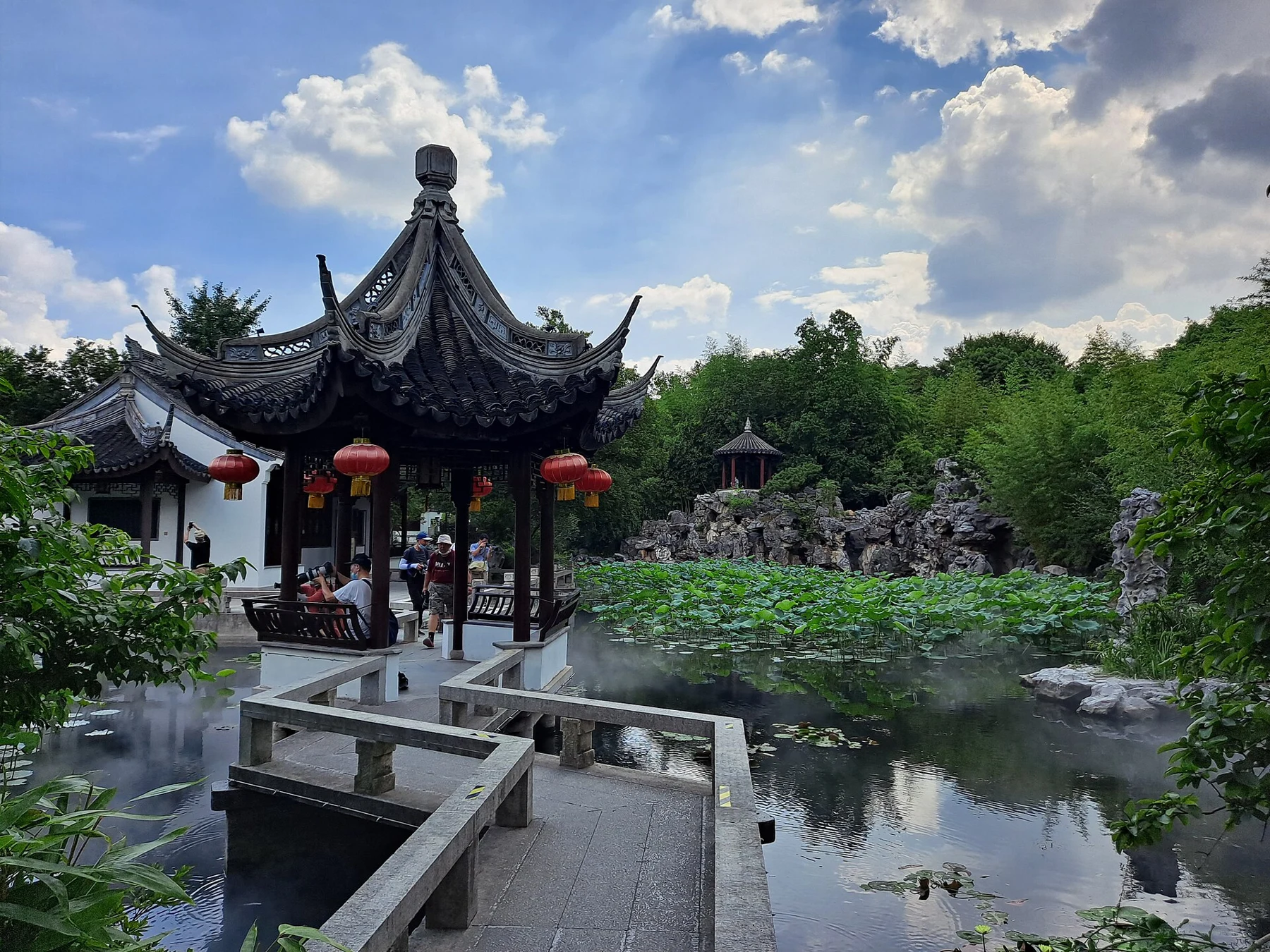 A small open pavilion reached by angular stone-railed paths across a lotus pond.