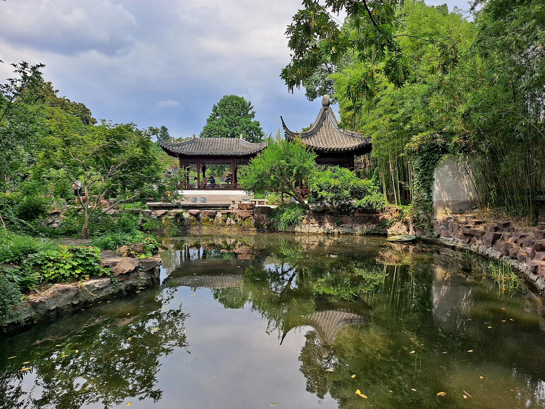 A small pond reflecting low pavilions and dense garden planting.