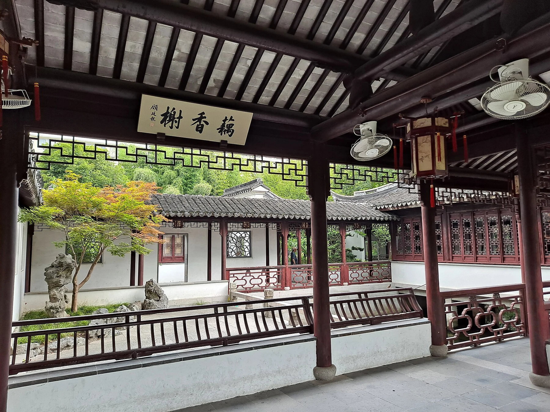 Dark roof beams and red columns framing white walls, lattice windows and a courtyard tree.