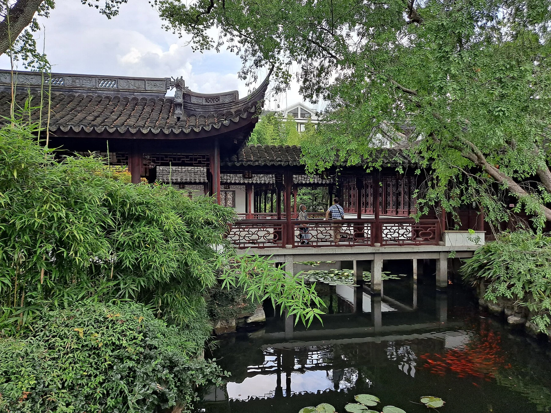 Bamboo beside a timber corridor raised over water, with red columns and carved rails.