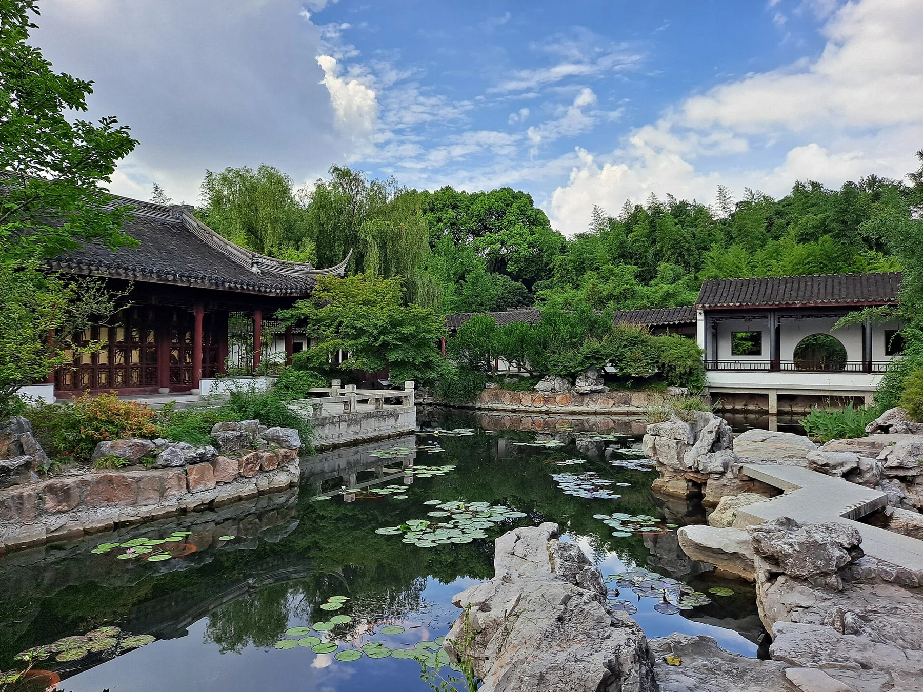 Low rock edges around water reflecting white-walled and timber garden buildings.