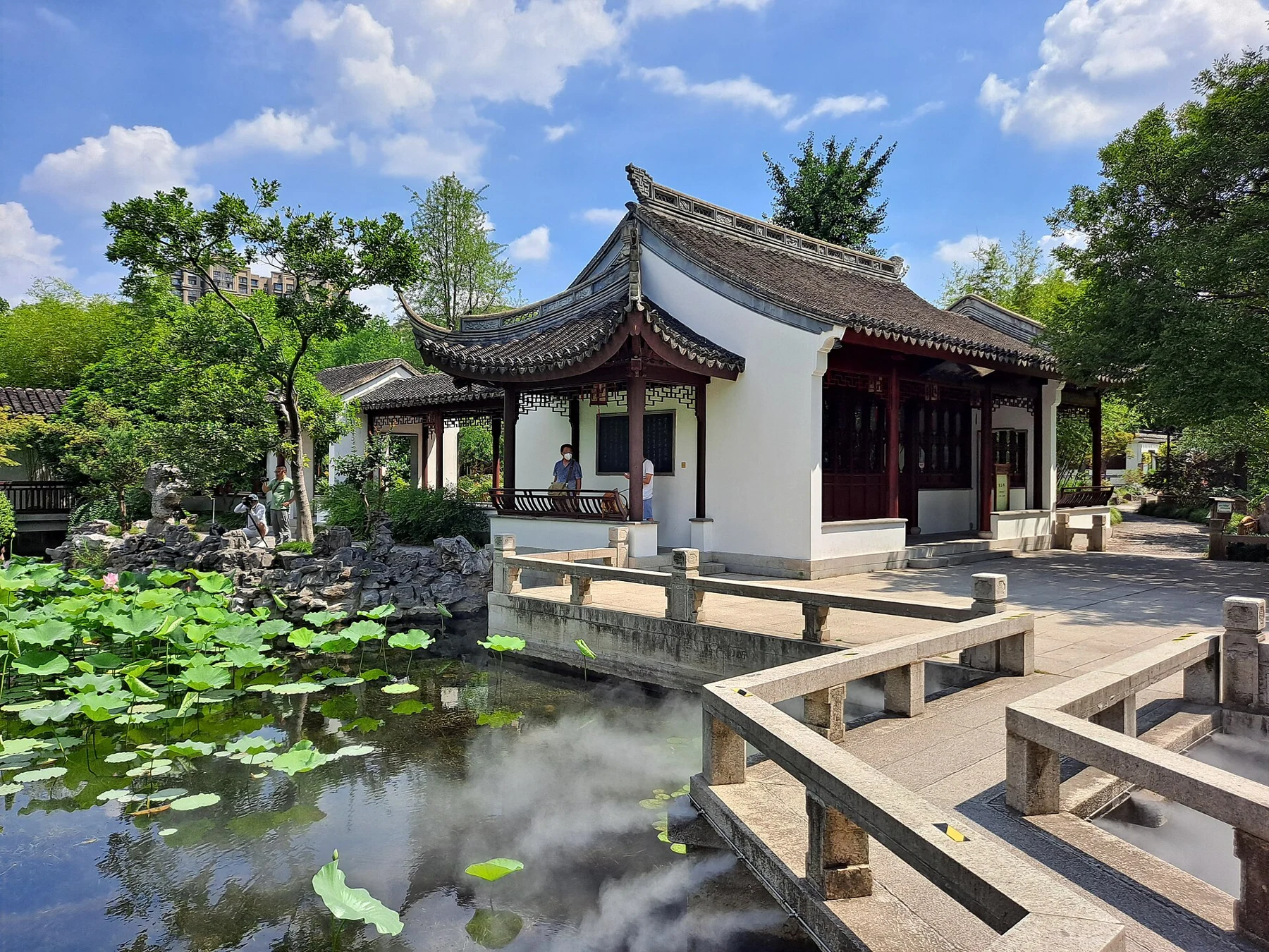 Angled stone rails, lotus leaves and a white-walled building reflected in the pond.