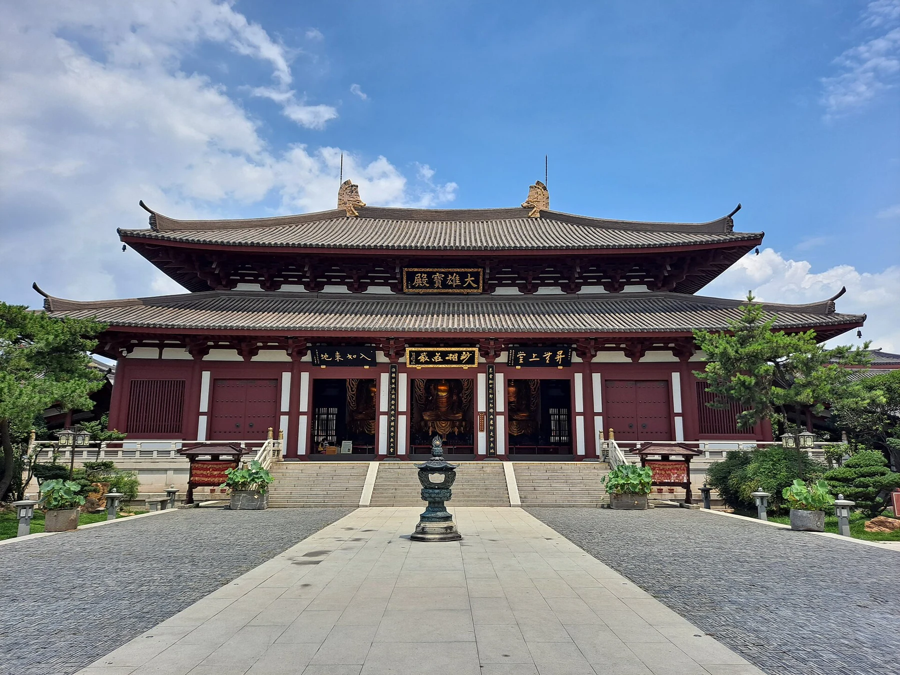 A broad red-columned main hall with a tiered tiled roof and stairs from the courtyard.