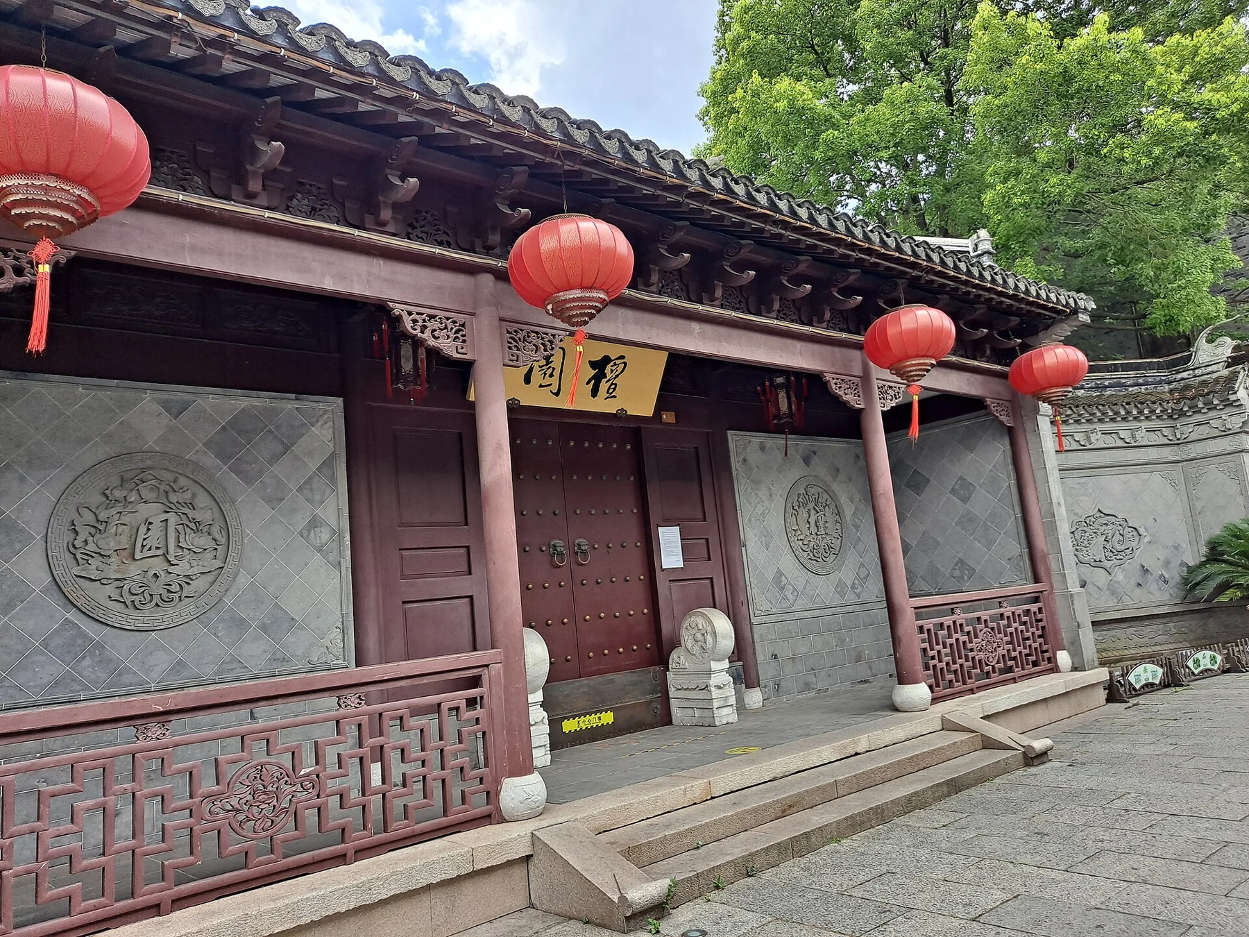 A red-and-grey garden frontage with circular carved panels, a doorway sign and red lanterns.
